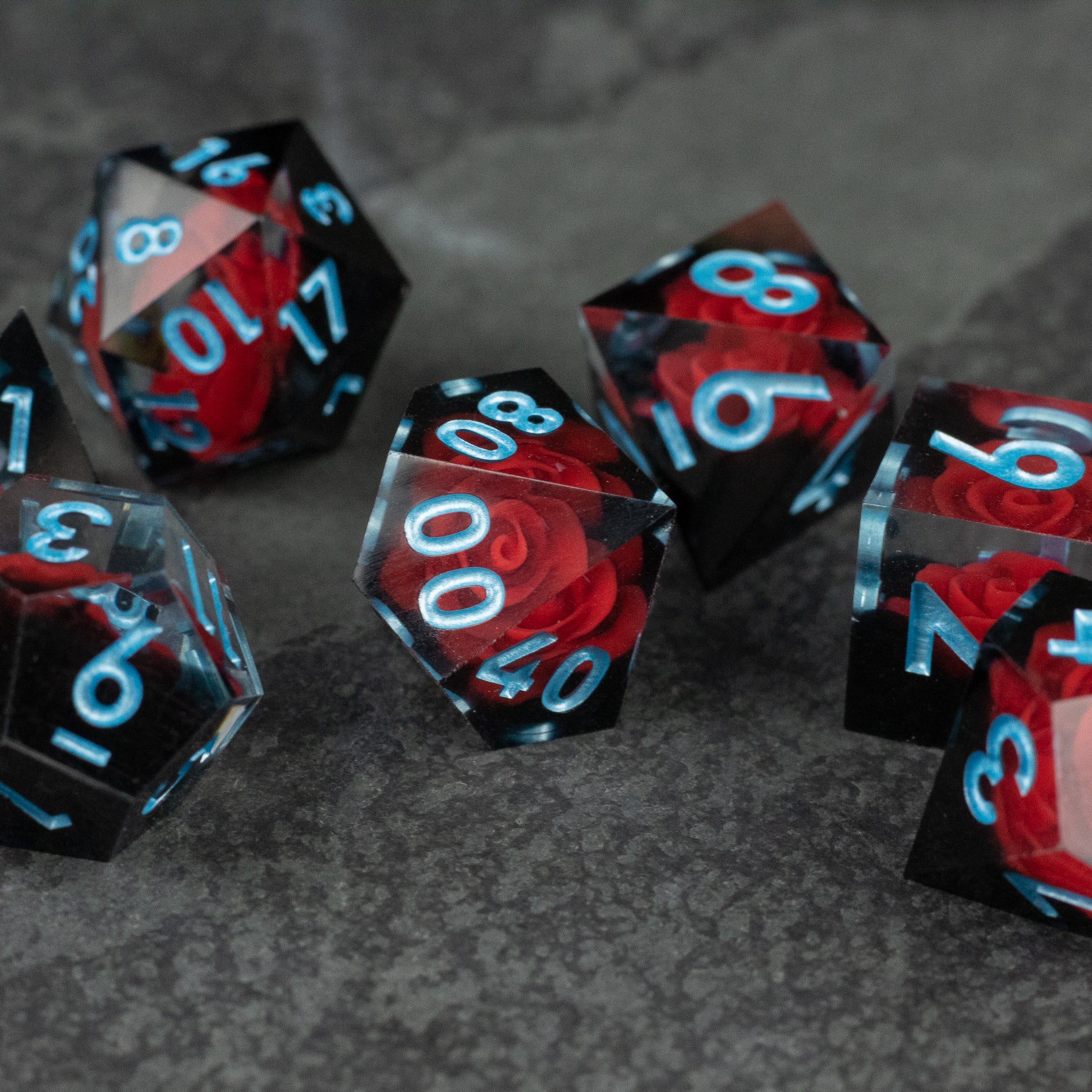 Cursed Rose Dice Set - Sharp-edged red and black translucent dice set with bright blue numbers on a dark surface.