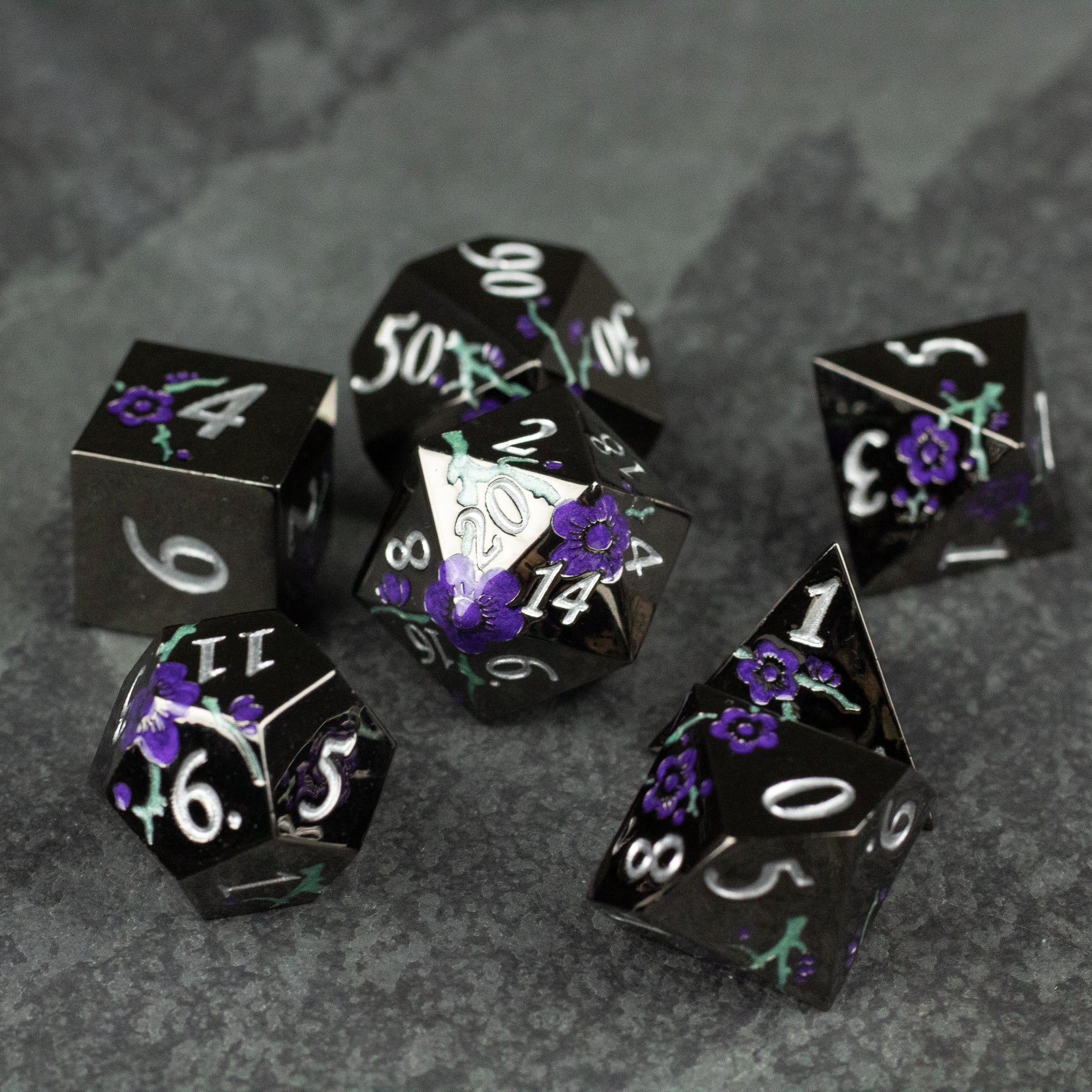 Black and Purple Metal Flower Dice - Set of black metal polyhedral dice with white numbers and purple flower designs on each face.
