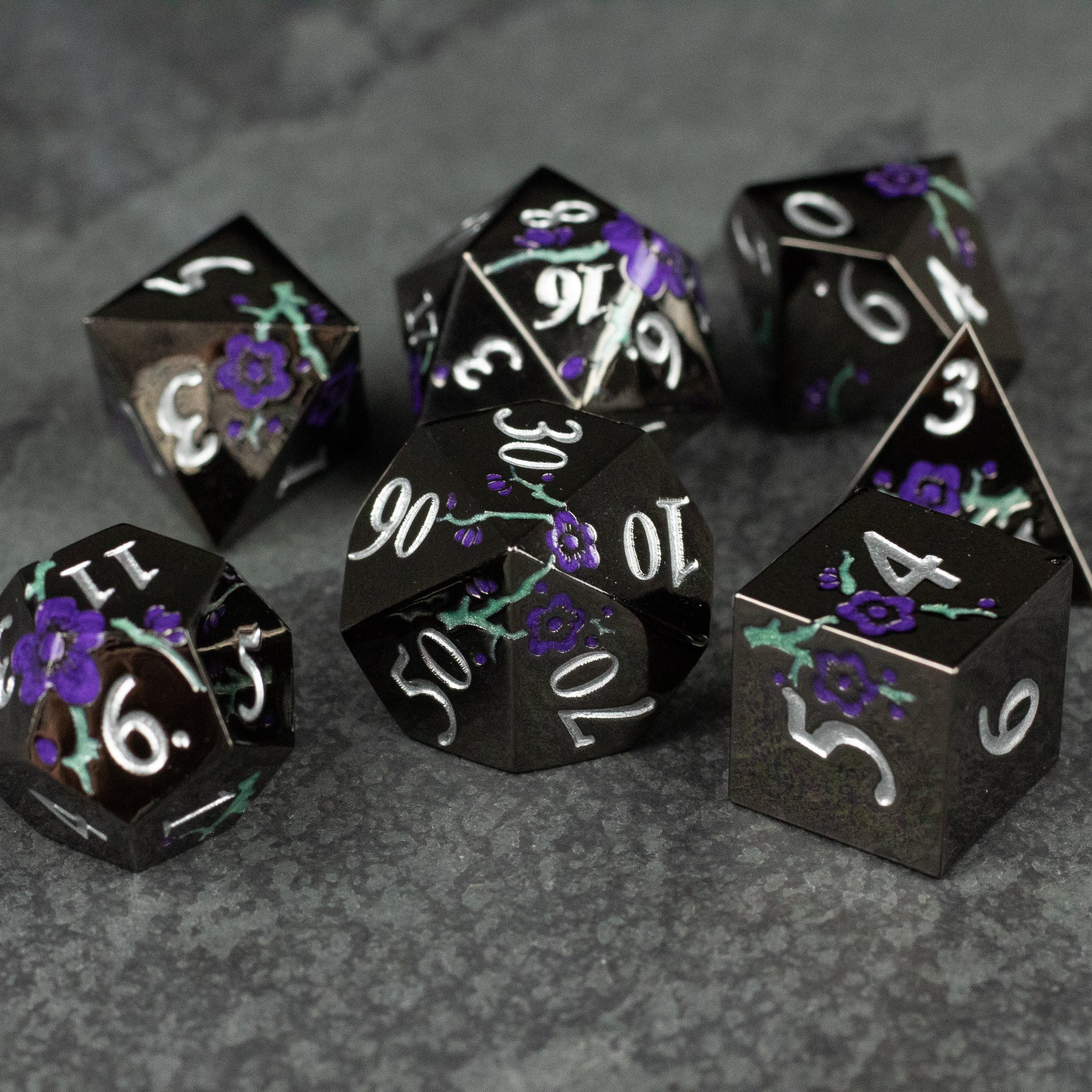 Black and Purple Metal Flower Dice - Set of seven black metal dice with white numbers and intricate purple flower designs.