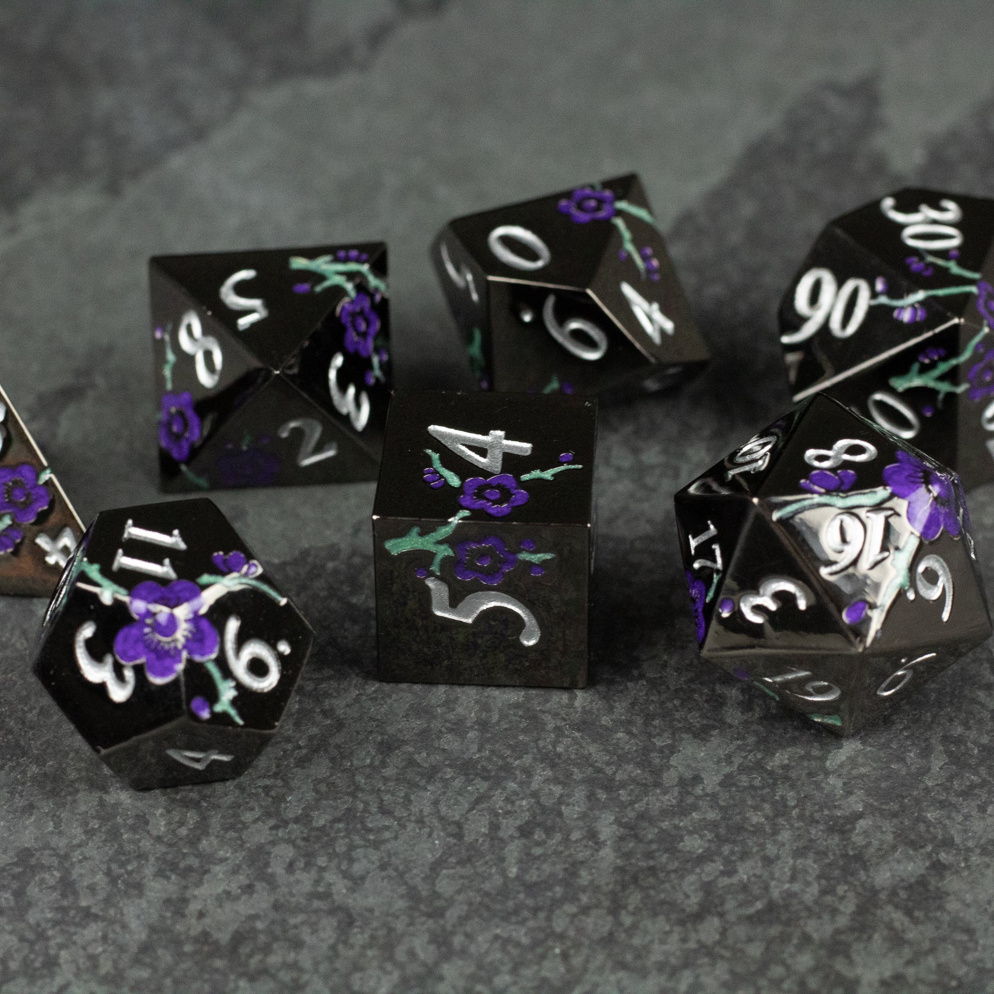 Black and Purple Metal Flower Dice - Set of black metal polyhedral dice with white numbers and purple flower designs accented with green leaves.