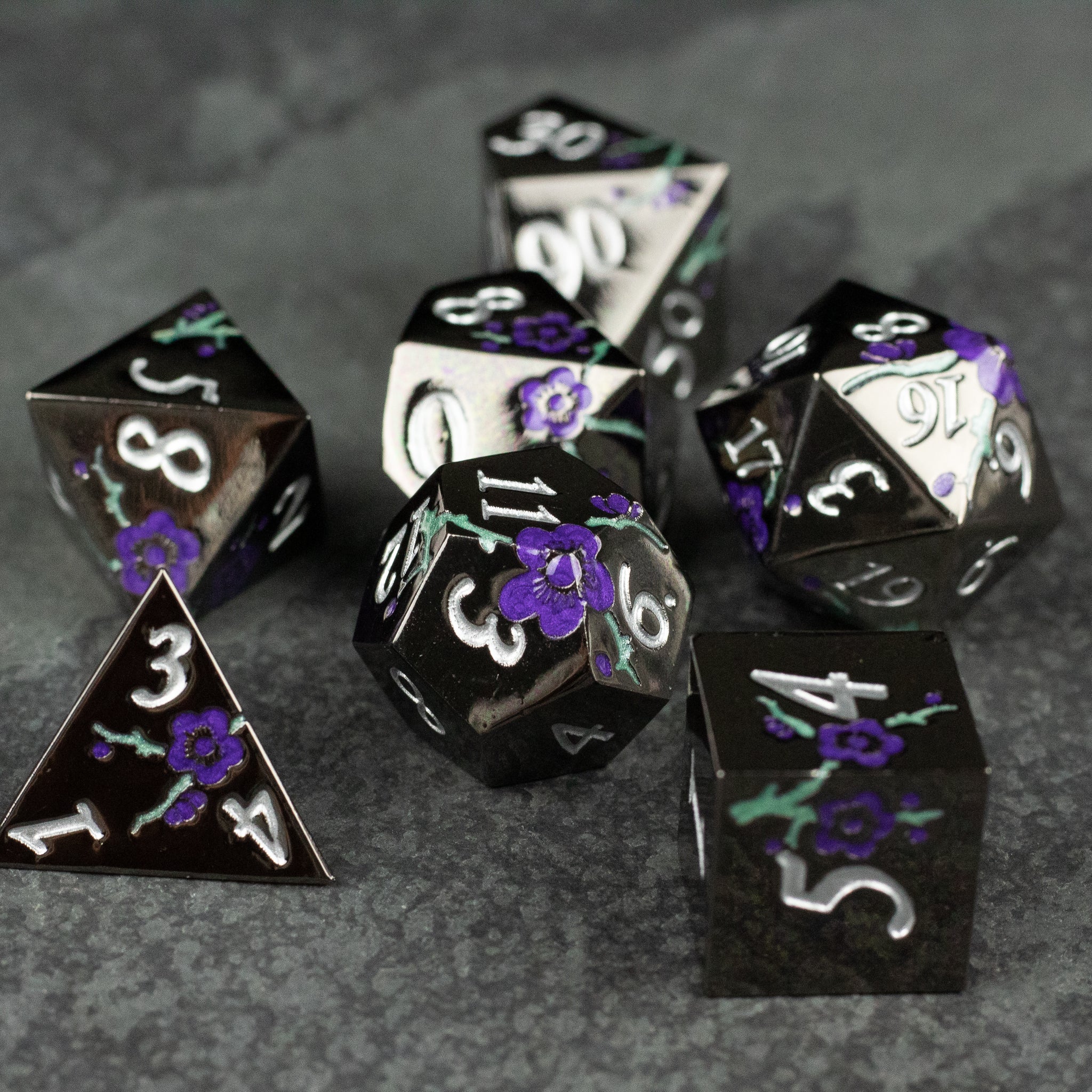 Black and Purple Metal Flower Dice - Set of black metal polyhedral dice with purple floral engravings and white numbering, including d4, d6, d8, d10, d12, and.