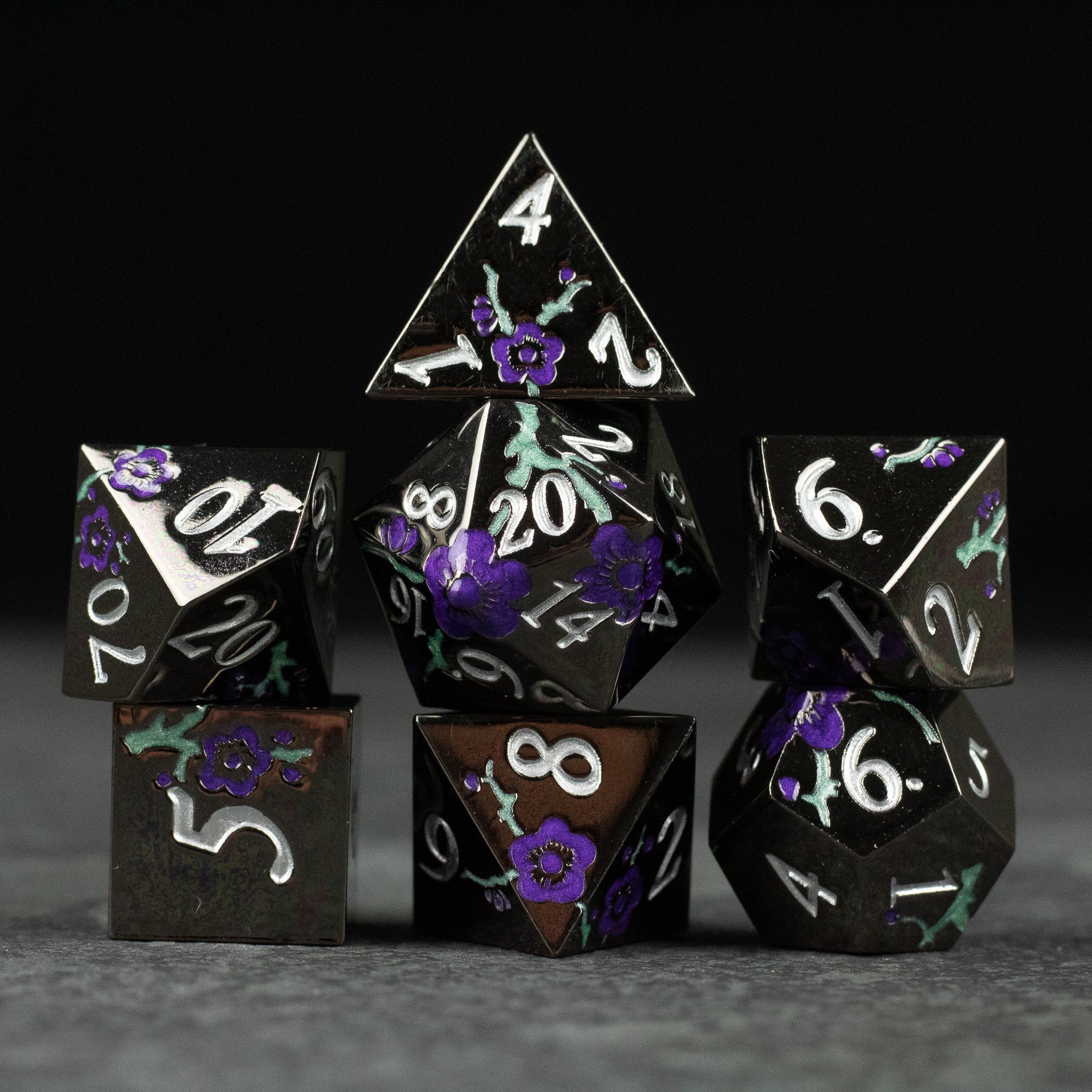 Black and Purple Metal Flower Dice - Set of seven black metal polyhedral dice with purple floral accents and white numbering for tabletop gaming.