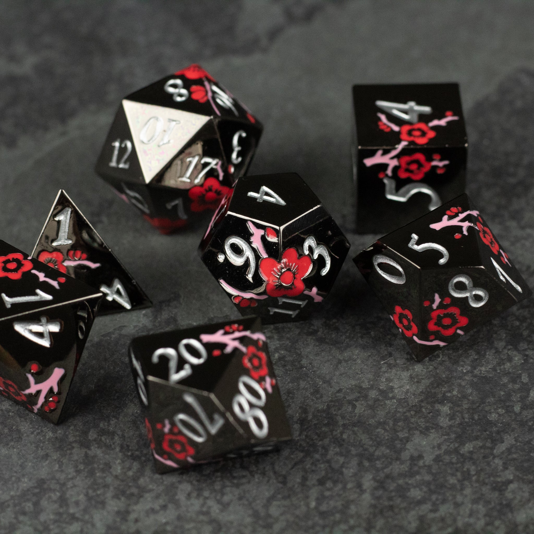 Black & Red Metal Flower Dice - Set of black metal polyhedral dice with red floral designs and white numbering on a dark textured surface.