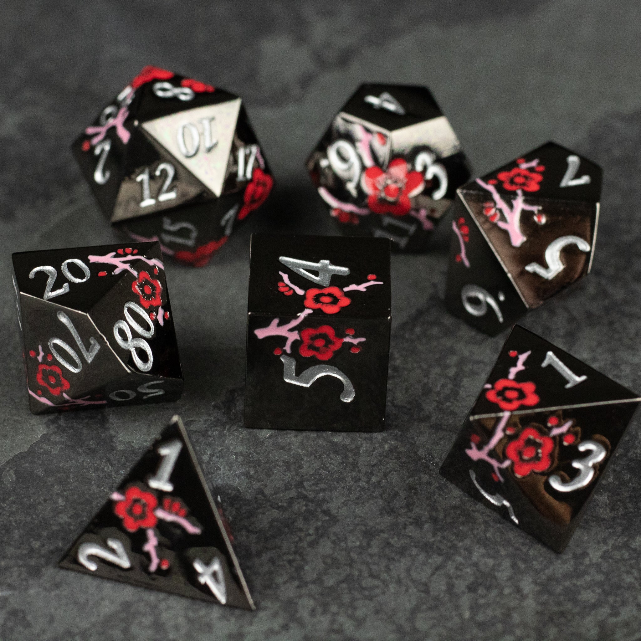 Black & Red Metal Flower Dice - Set of black metal dice with red flower designs and white numbering, featuring various polyhedral shapes.