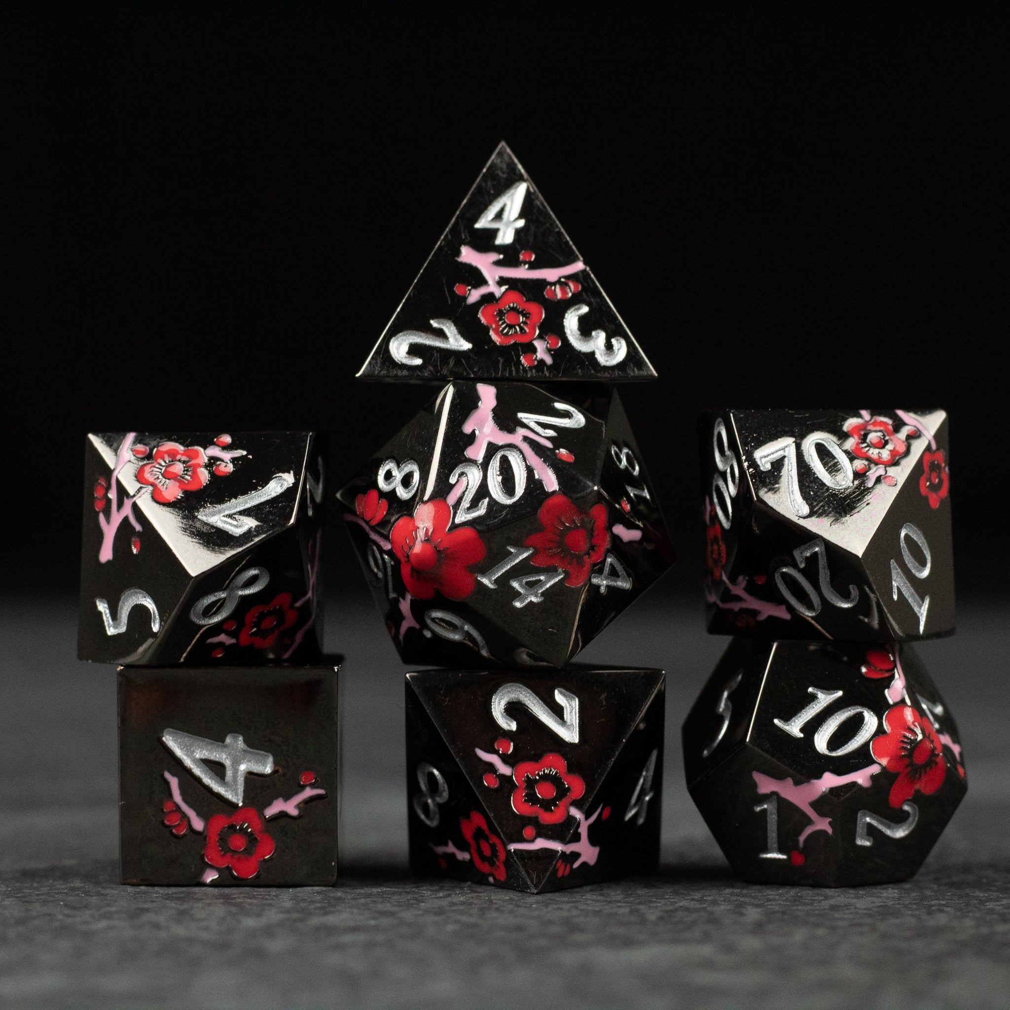 Black & Red Metal Flower Dice - Set of seven black metal dice with red floral designs and white numbers, including d4, d6, d8, d10, d12, and d20 shapes.