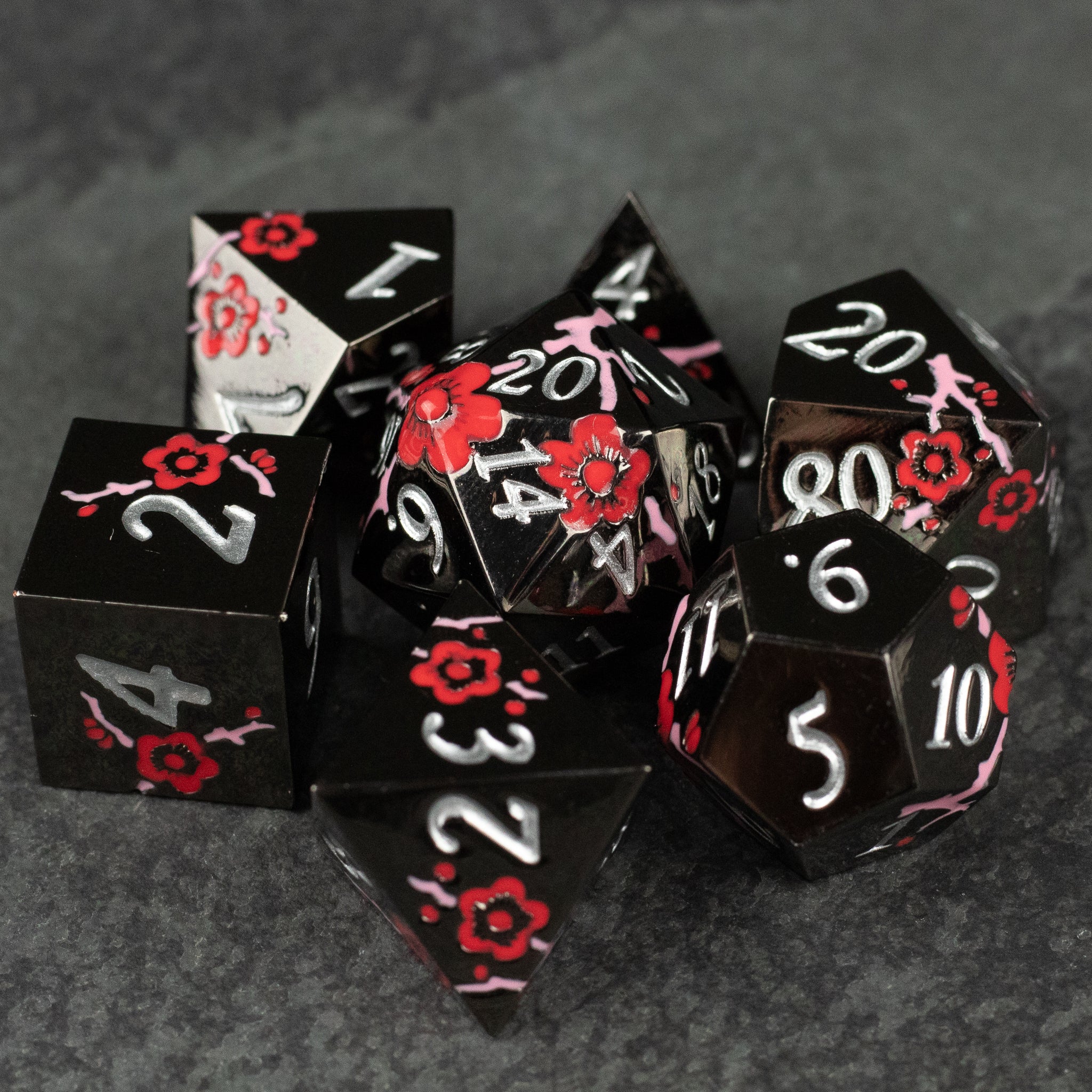 Black & Red Metal Flower Dice - Set of black metal dice with red flower engravings and white numbering, including d4, d6, d8, d10, d12, and d20 shapes.