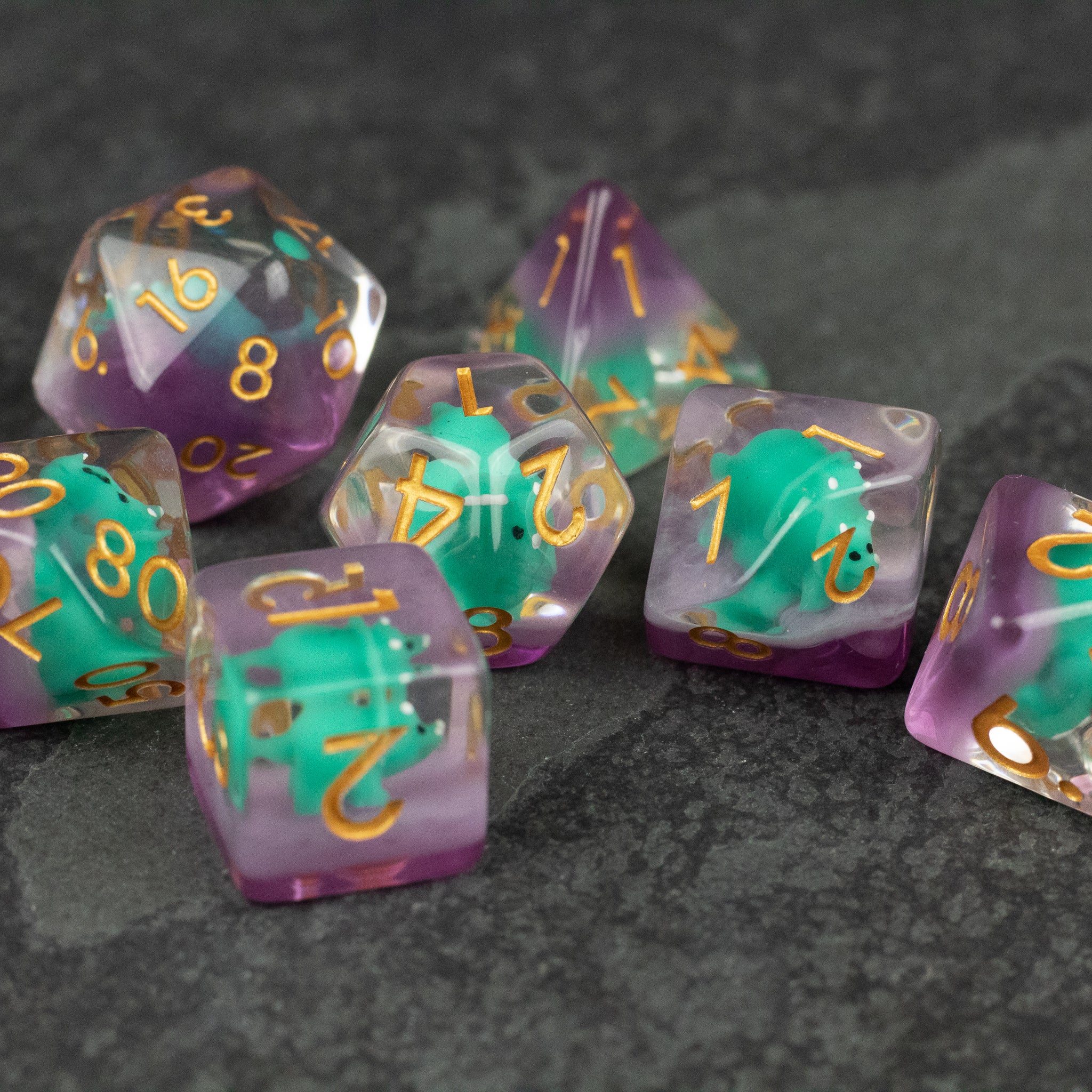 Green Triceratops Dice Set - Set of ten green and purple translucent polyhedral dice with gold numbers on a dark textured surface.
