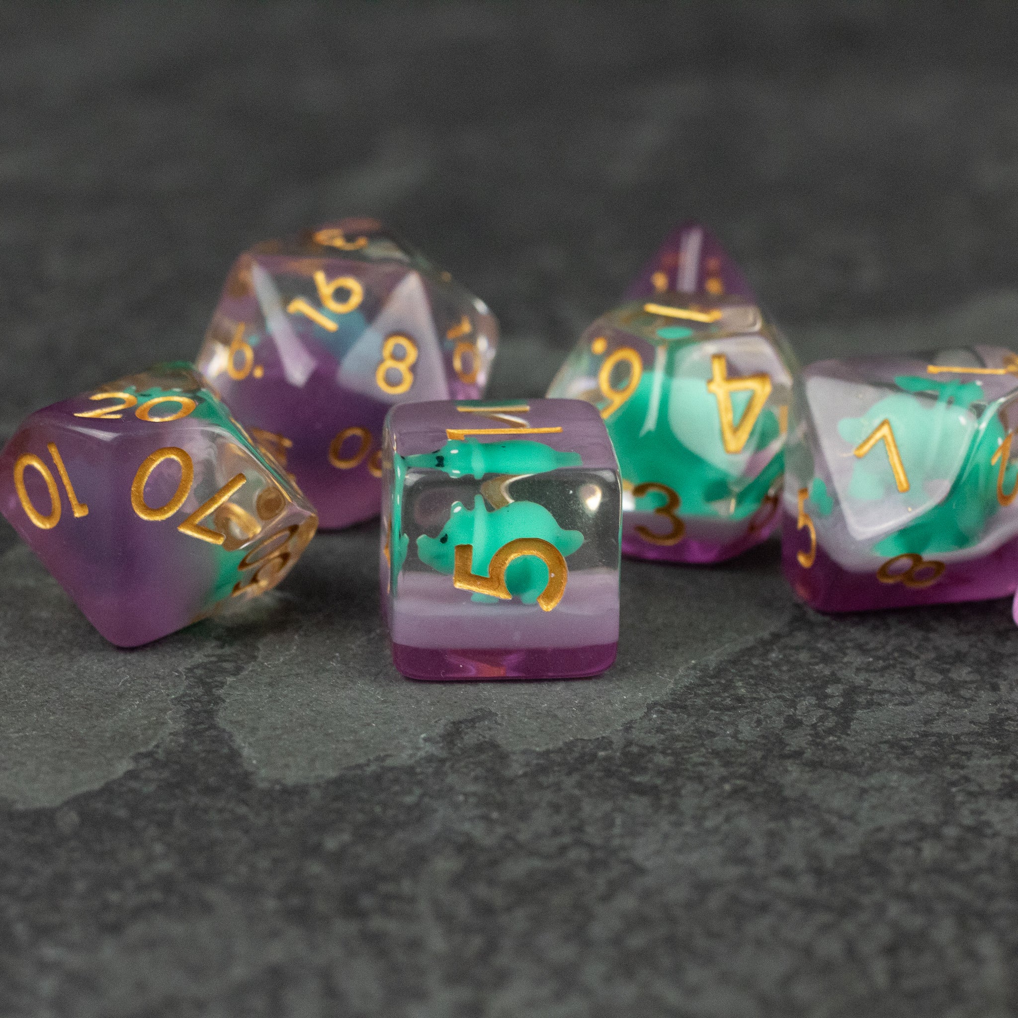 Green Triceratops Dice Set - Set of translucent purple and green polyhedral dice with gold numbers, featuring a unique triceratops-inspired design.