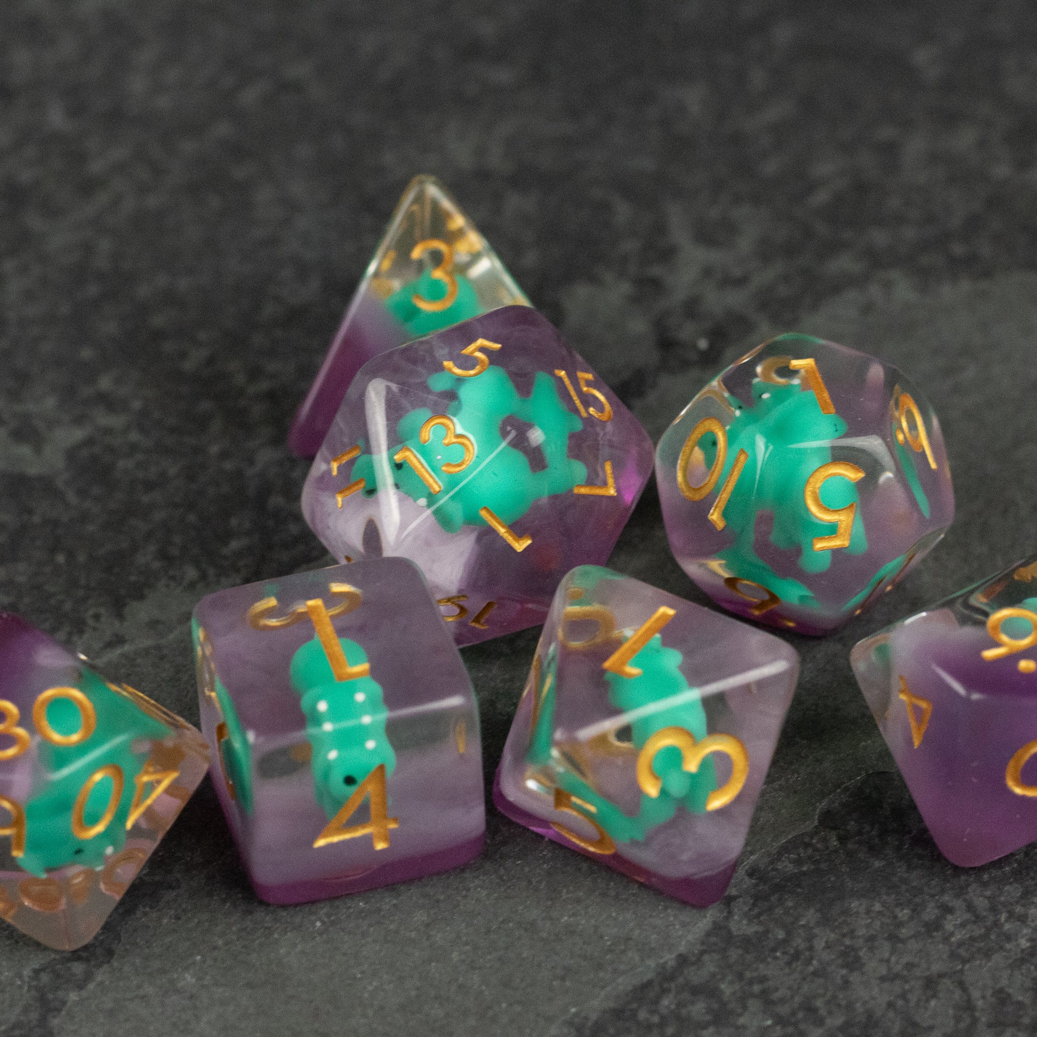 Green Triceratops Dice Set - Seven translucent polyhedral dice with green and purple swirls and gold numbers, including a d20, d12, d10, d8, d6, and d4.