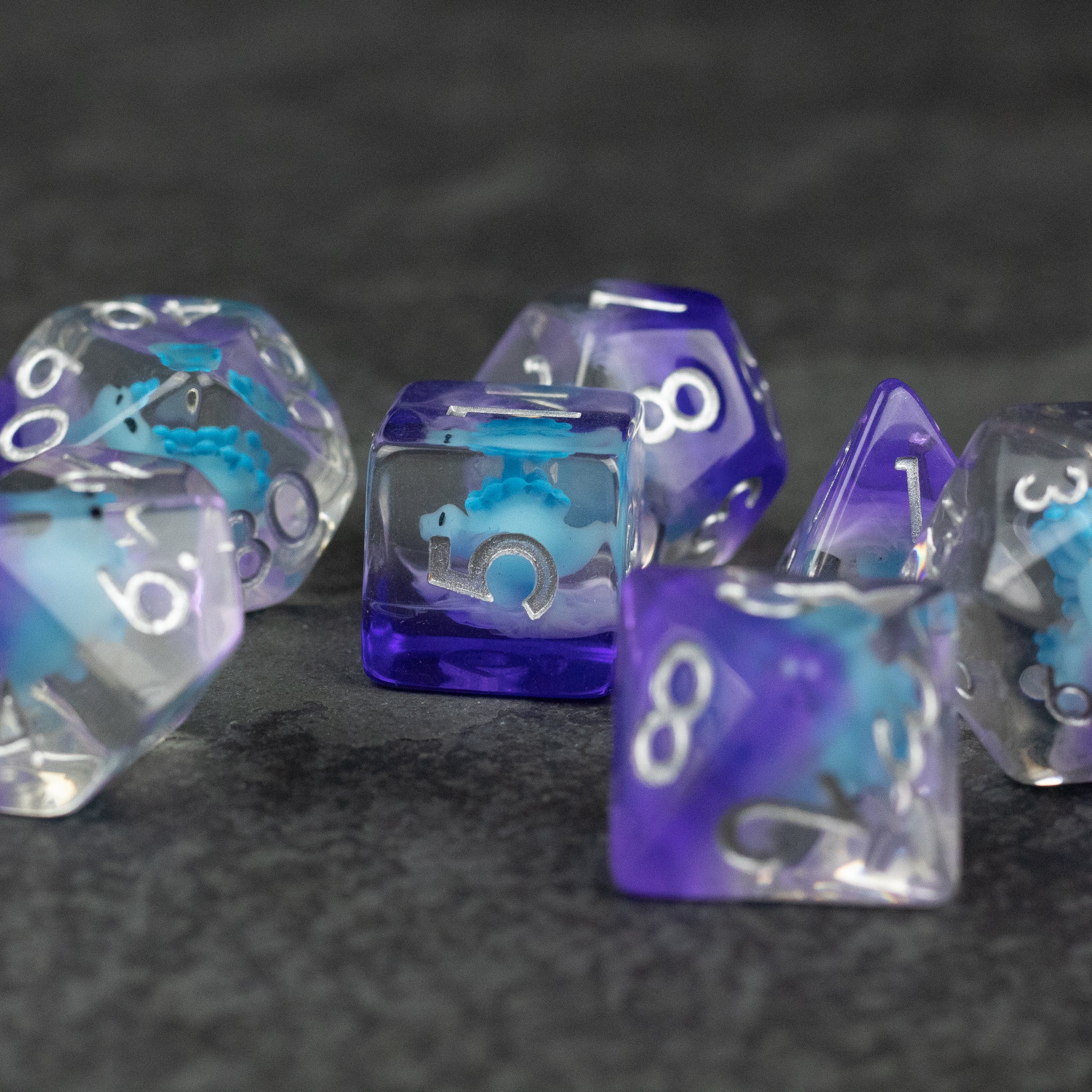 Blue Stegosaurus Dice Set - Blue and purple translucent polyhedral dice with white numbers and a small stegosaurus figure inside each die.