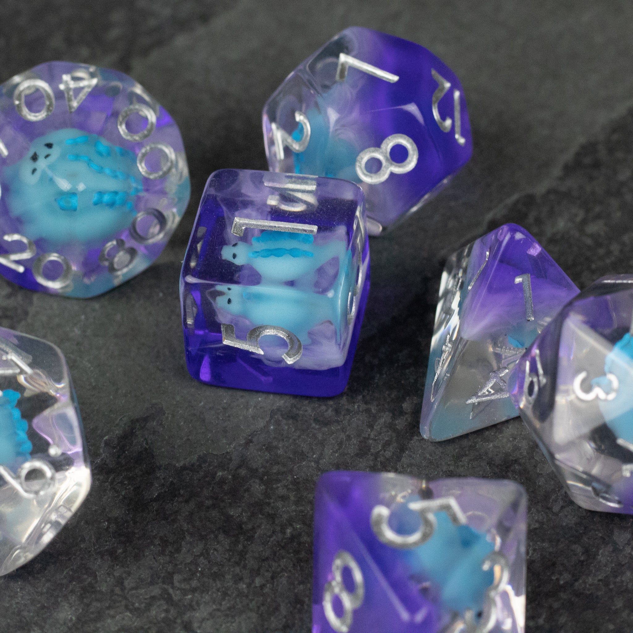 Blue Stegosaurus Dice Set - Set of translucent blue and purple polyhedral dice with embedded blue stegosaurus figures and white numbering on dark surface.
