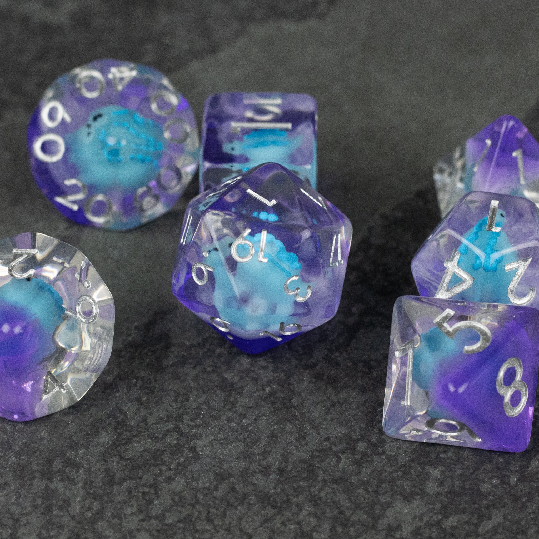 Blue Stegosaurus Dice Set - Set of translucent blue and purple polyhedral dice with white numbers, featuring a small stegosaurus figure inside each die.