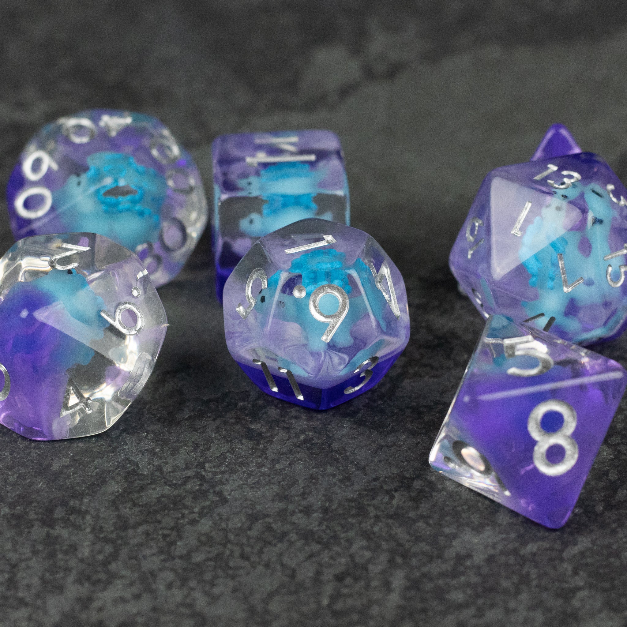 Blue Stegosaurus Dice Set - Set of translucent blue and purple polyhedral dice with white numbering on a dark textured surface.