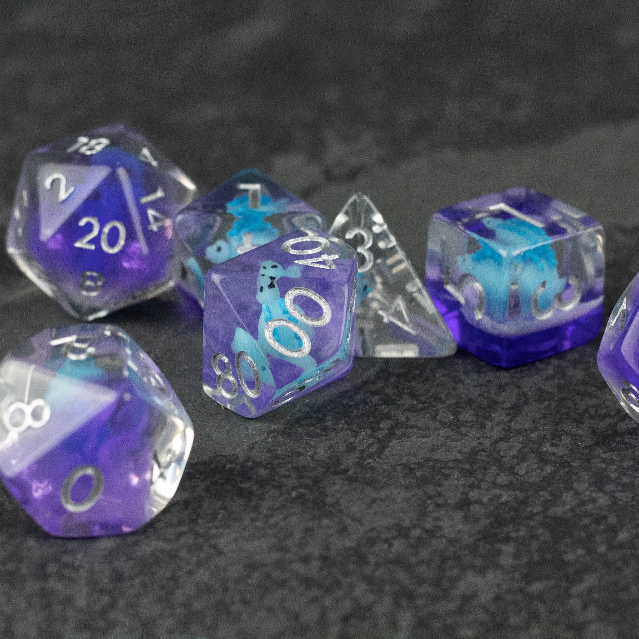 Blue Stegosaurus Dice Set - Set of seven translucent blue and purple polyhedral dice with white numbers, including d20, d12, d10, d8, d6, and d4 shapes.