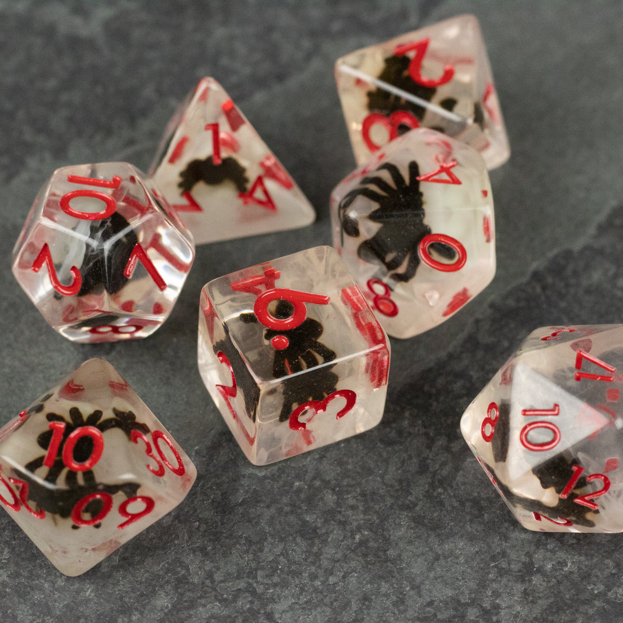 Black Spider Dice Set - White - Transparent dice set with red numbers and black spider designs inside on gray surface.