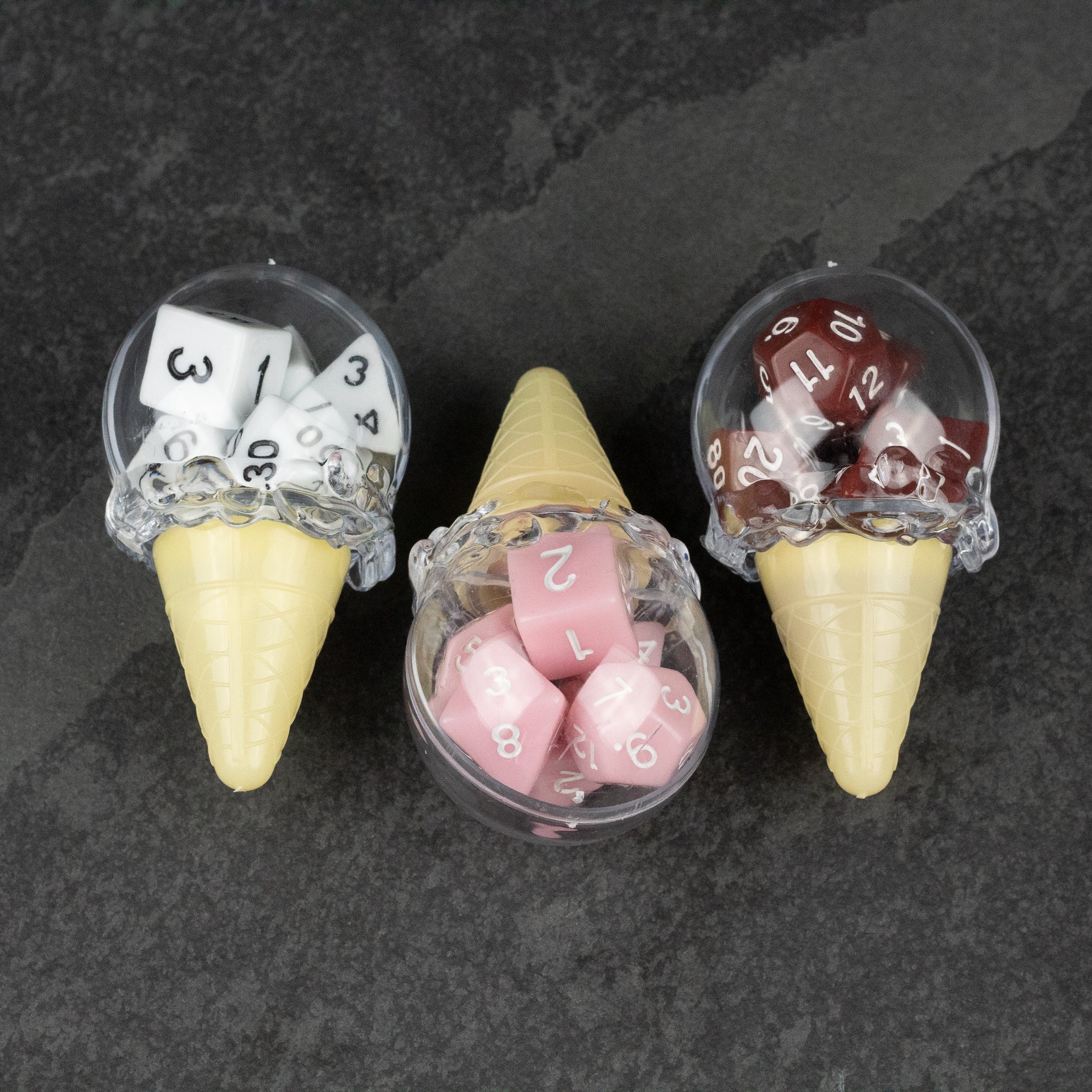Dice Cream Cones - Three plastic ice cream cones filled with translucent polyhedral dice in white, pink, and brown colors on a dark surface.