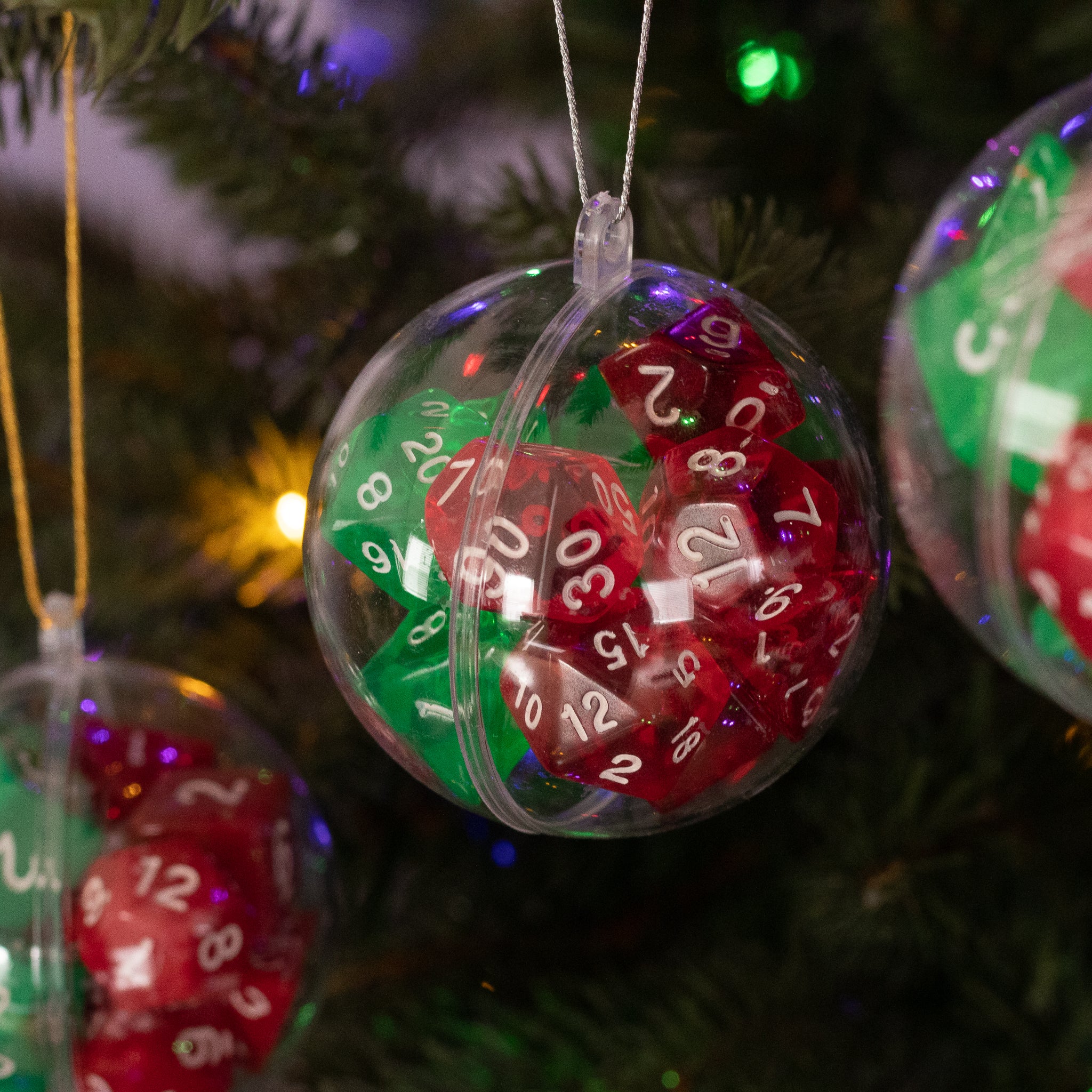 Christmas Dice Ball Ornaments - Clear spherical ornament containing red and green polyhedral dice with white numbers, hanging on tree branch.