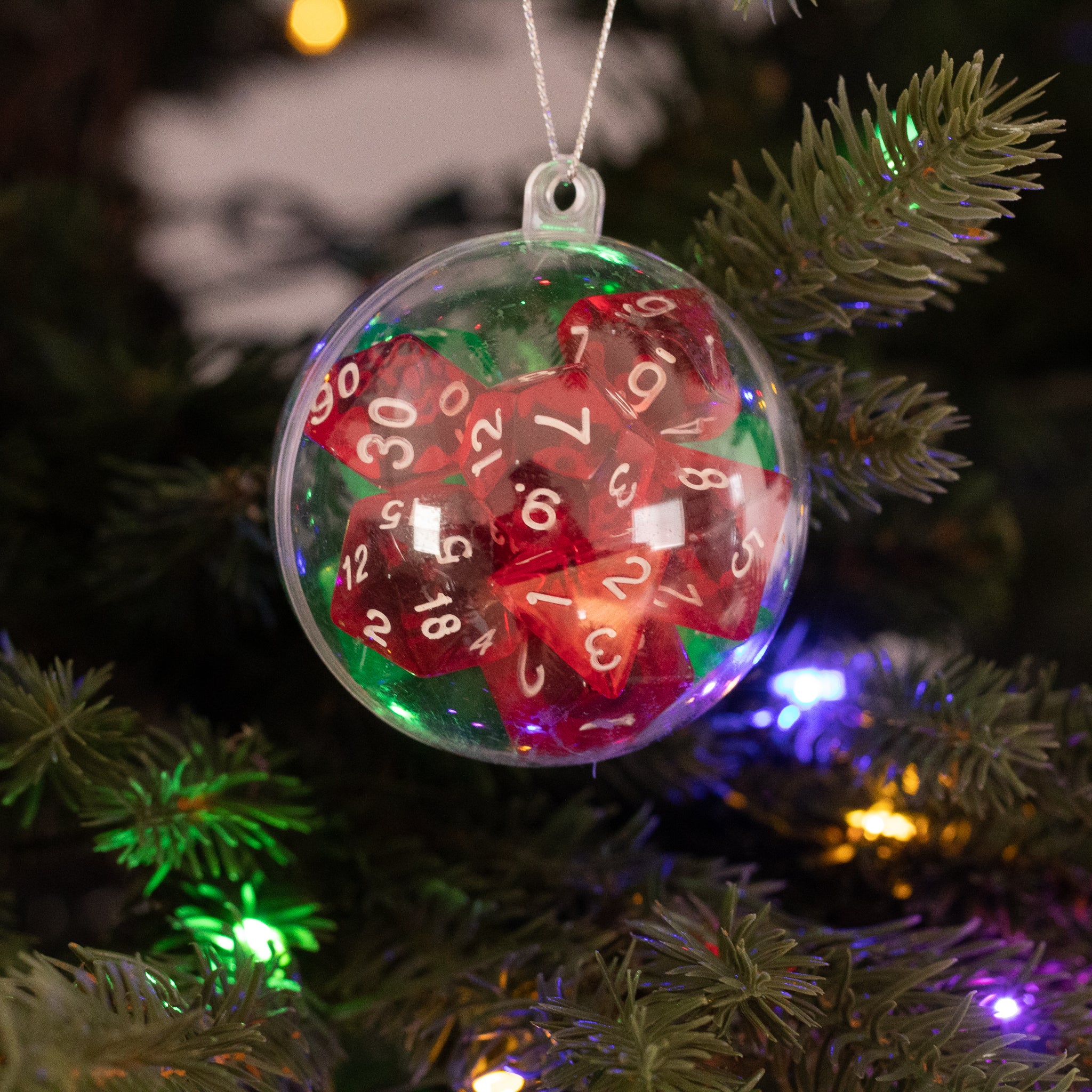 Christmas Dice Ball Ornaments - Clear spherical ornament filled with assorted red and green polyhedral gaming dice, hanging on a Christmas tree branch with.