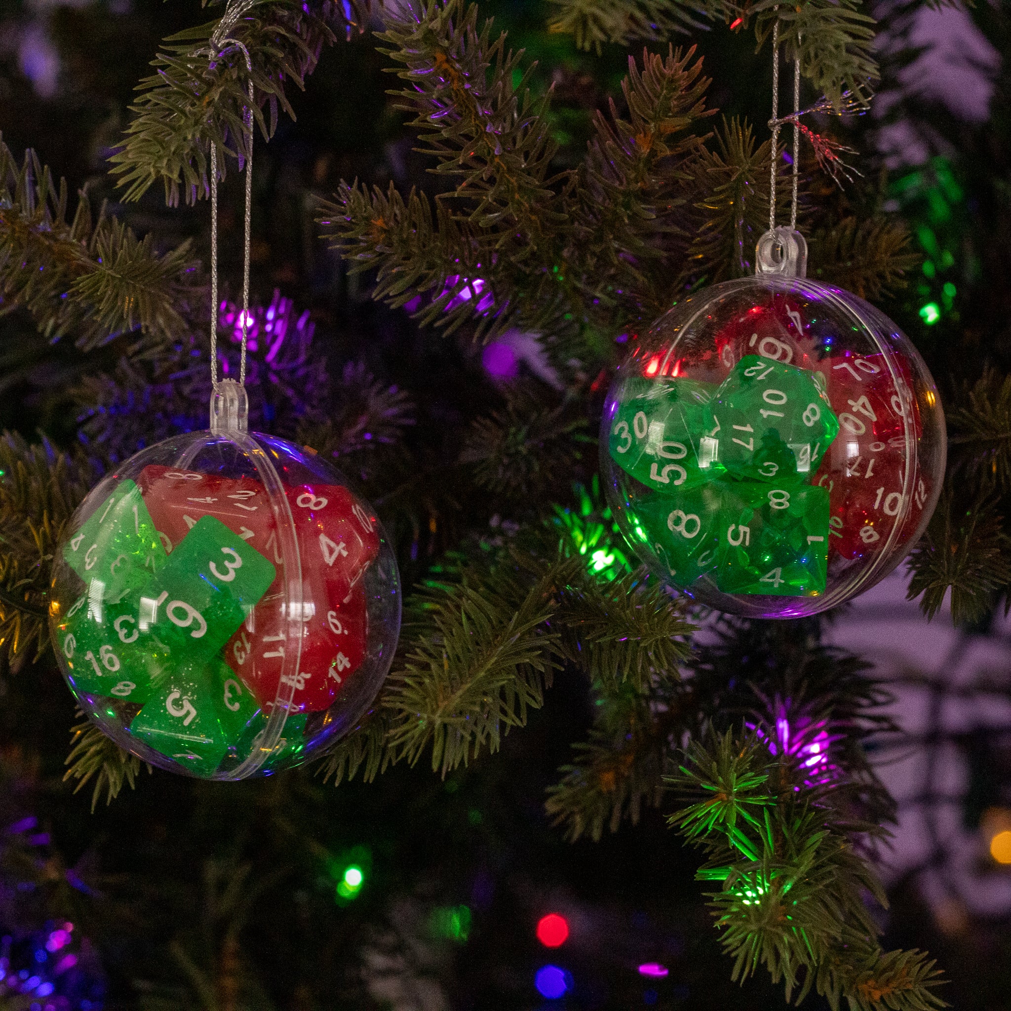 Christmas Dice Ball Ornaments - Clear plastic ball ornaments containing green and red polyhedral dice with white numbers hanging on a Christmas tree.