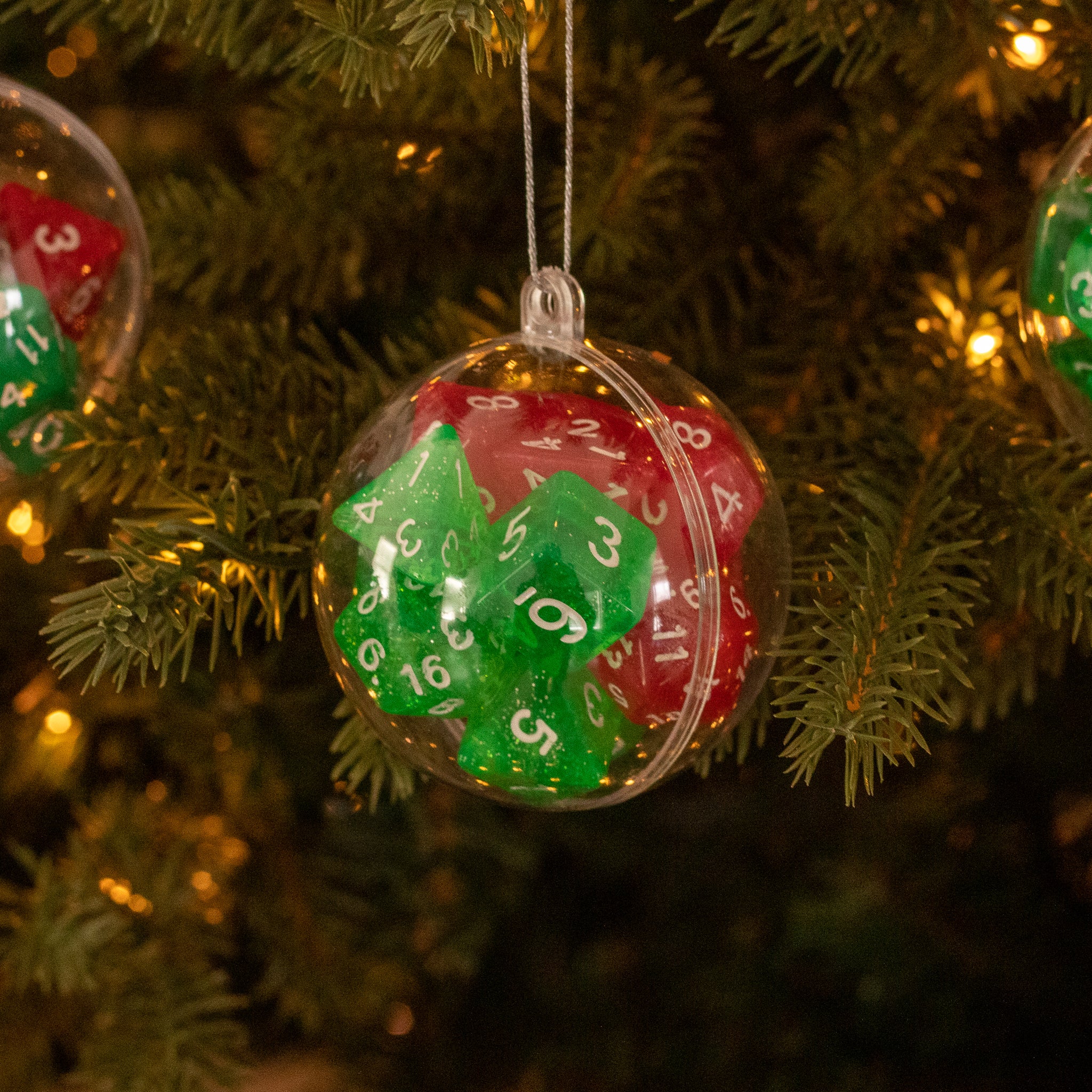 Christmas Dice Ball Ornaments - Clear round ornament ball filled with red and green 20-sided dice hanging on Christmas tree with warm lights.