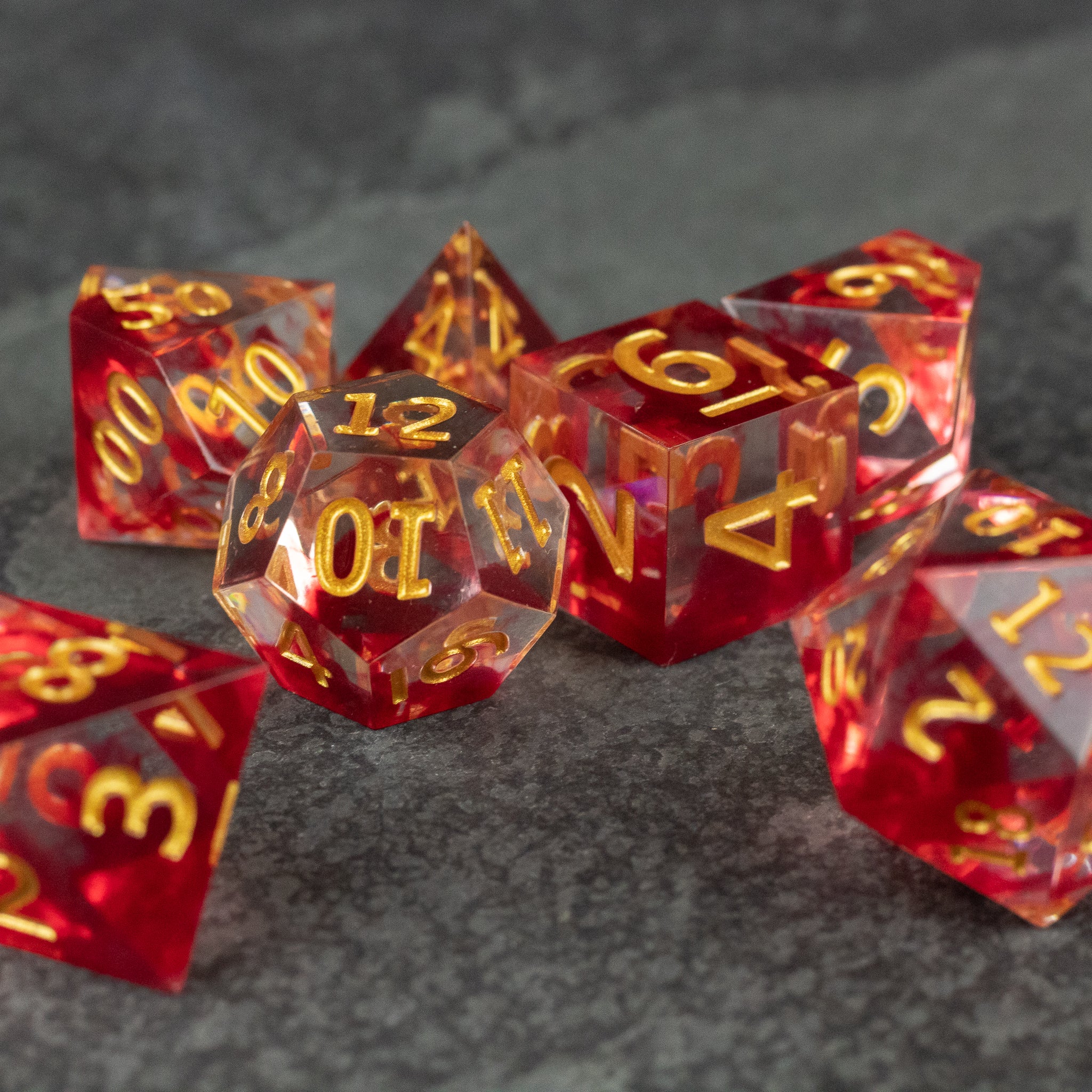 Blood Pact Dice Set - Translucent red sharp-edged dice set with gold numbering, including d20, d12, d10, d8, d6, and d4 shapes on dark textured.