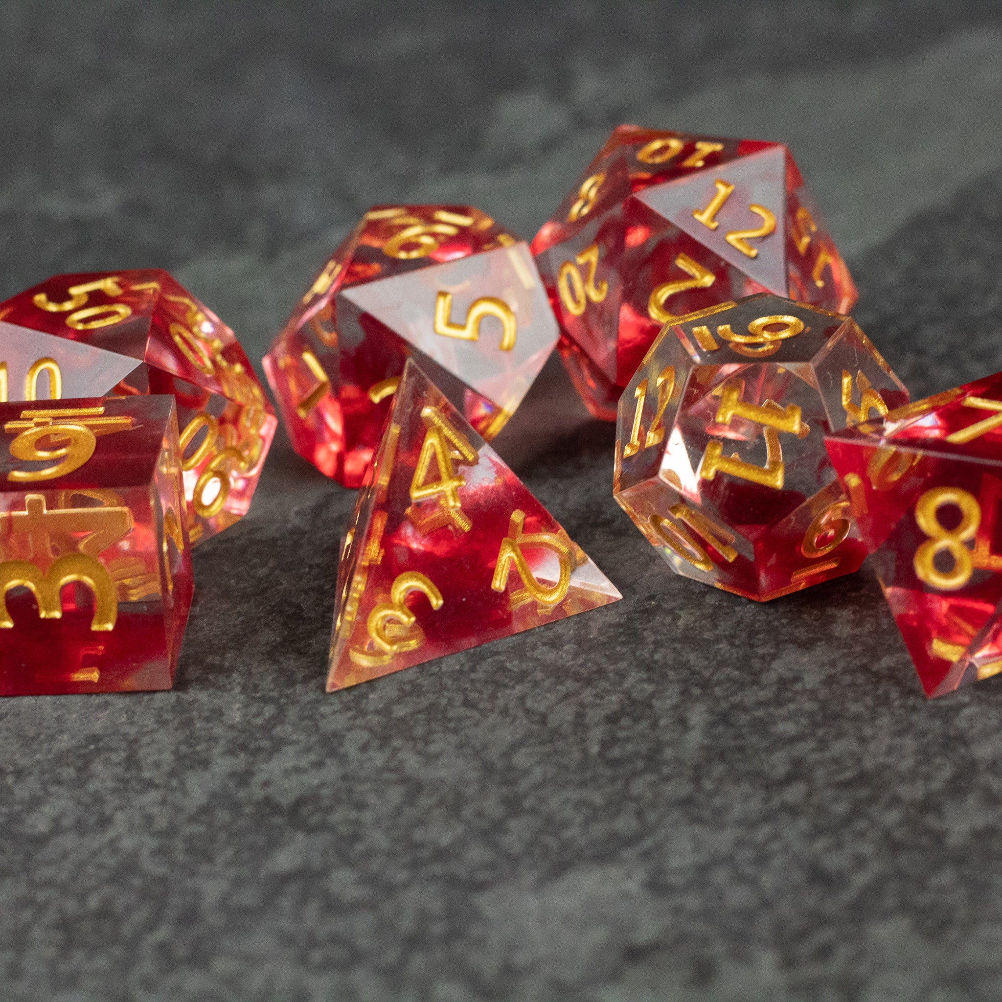 Blood Pact Dice Set - Red and clear sharp-edged polyhedral dice set with gold numbers, including d20, d12, d10, d8, d6, and d4.