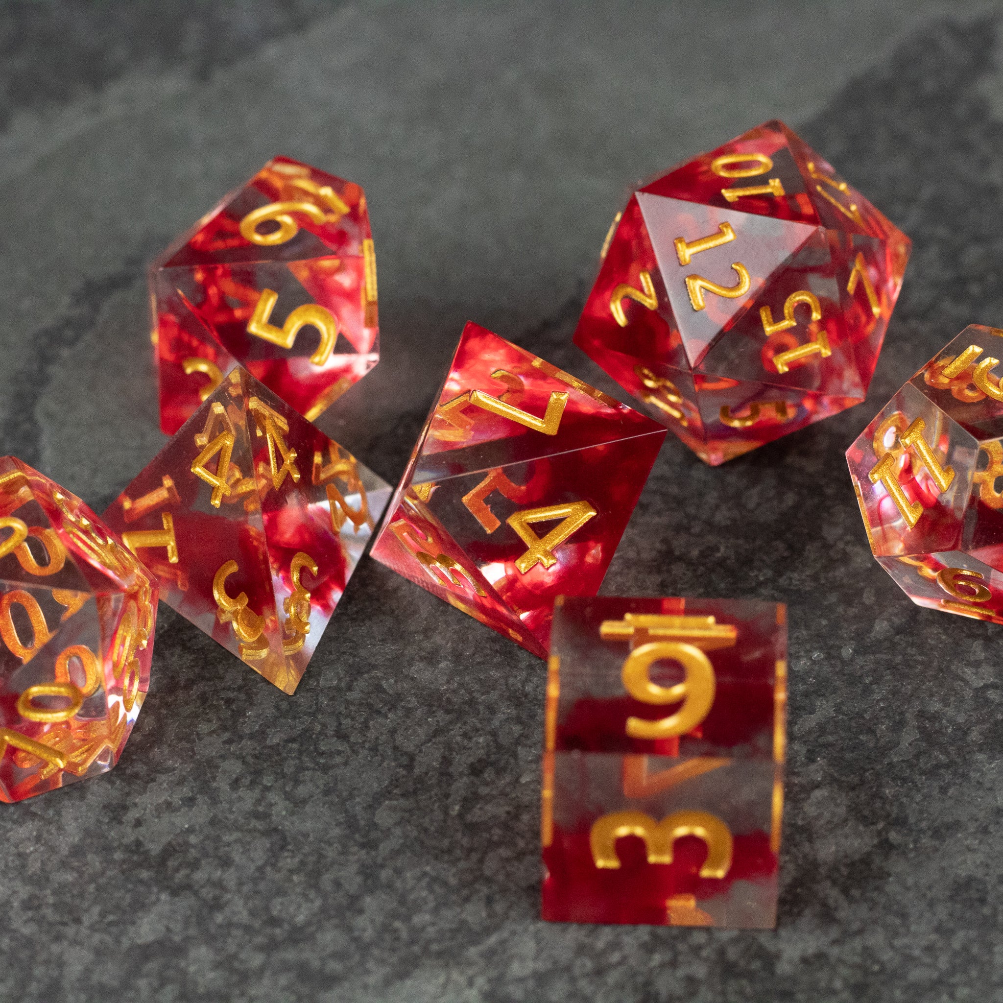 Blood Pact Dice Set - Translucent red sharp-edged polyhedral dice set with gold numbers on dark gray surface.