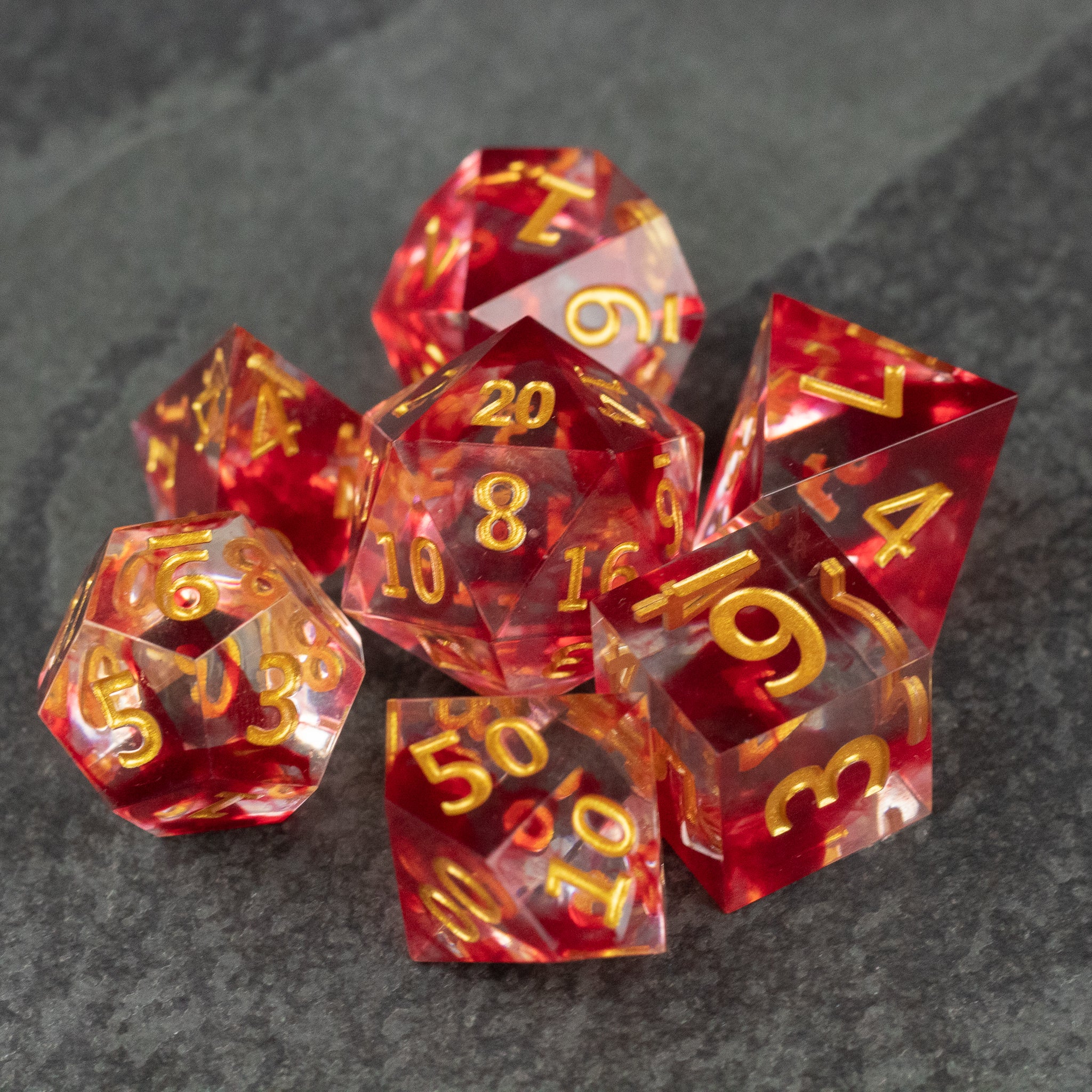 Blood Pact Dice Set - Set of seven translucent red polyhedral dice with sharp edges and gold numbering on a dark surface.