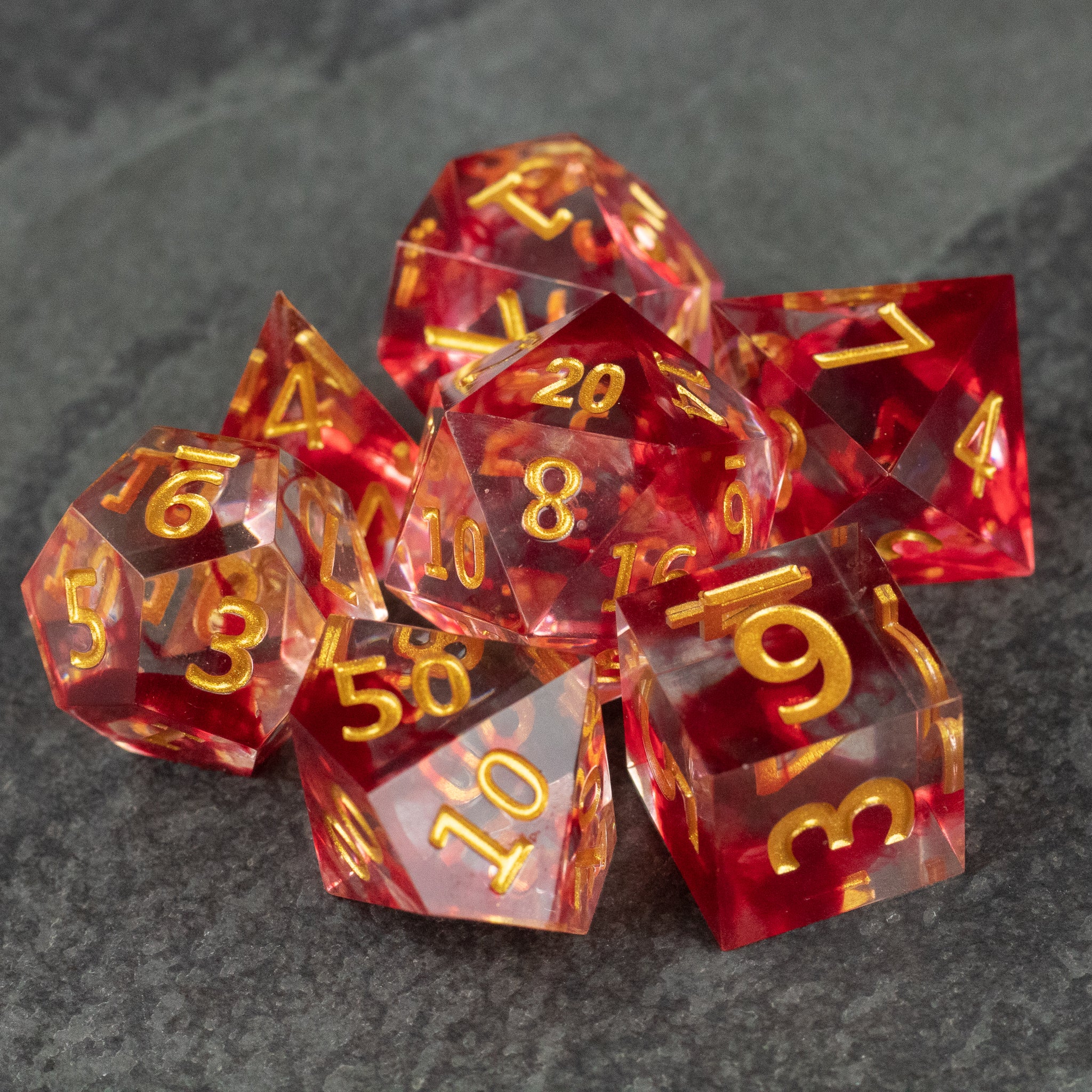Blood Pact Dice Set - Translucent red polyhedral dice set with sharp edges and gold numbering, includes d20, d12, d10, d8, d6, and d4.