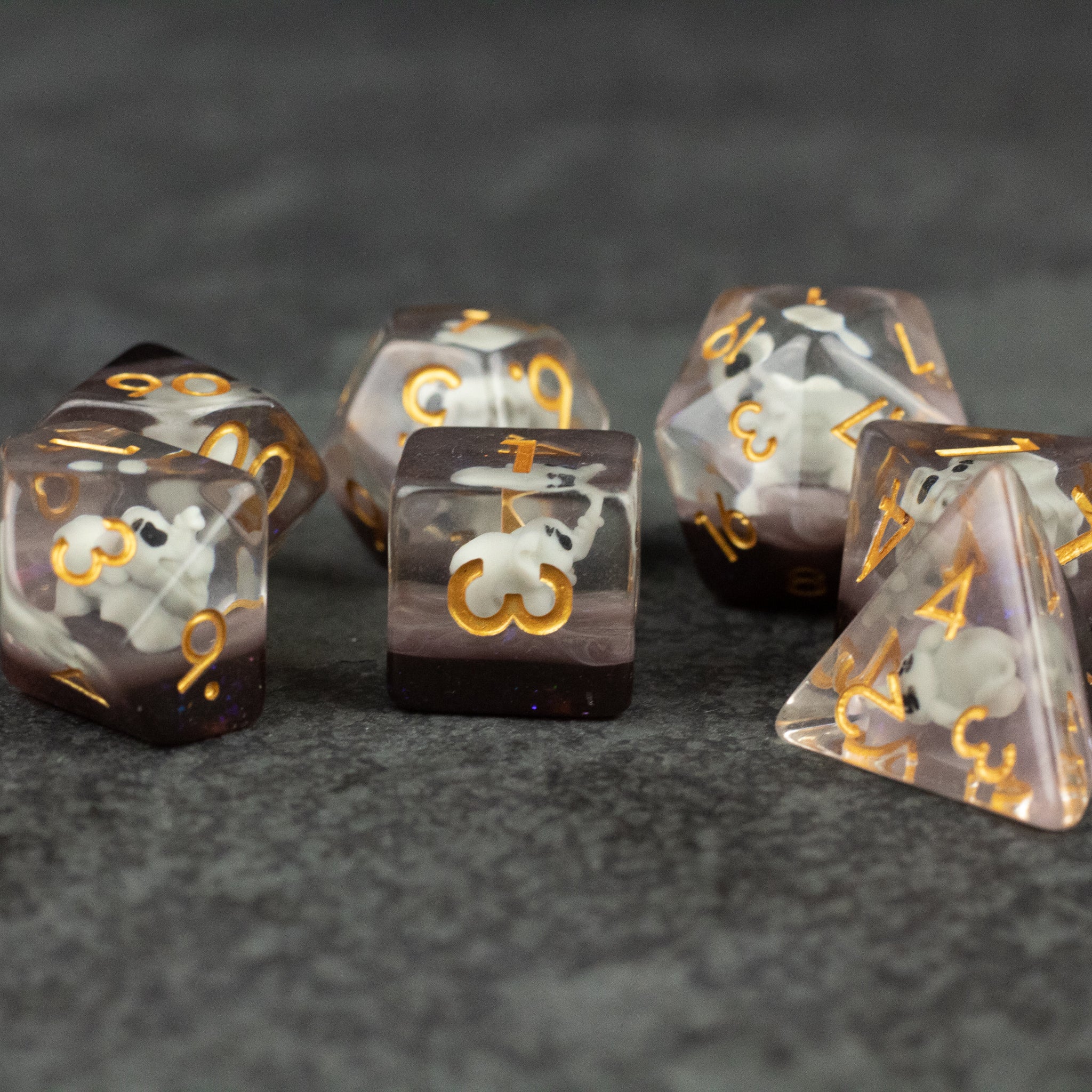 Elephant Dice Set - Set of seven translucent smoky gray polyhedral dice with gold numbers and elephant icons on a dark textured surface.