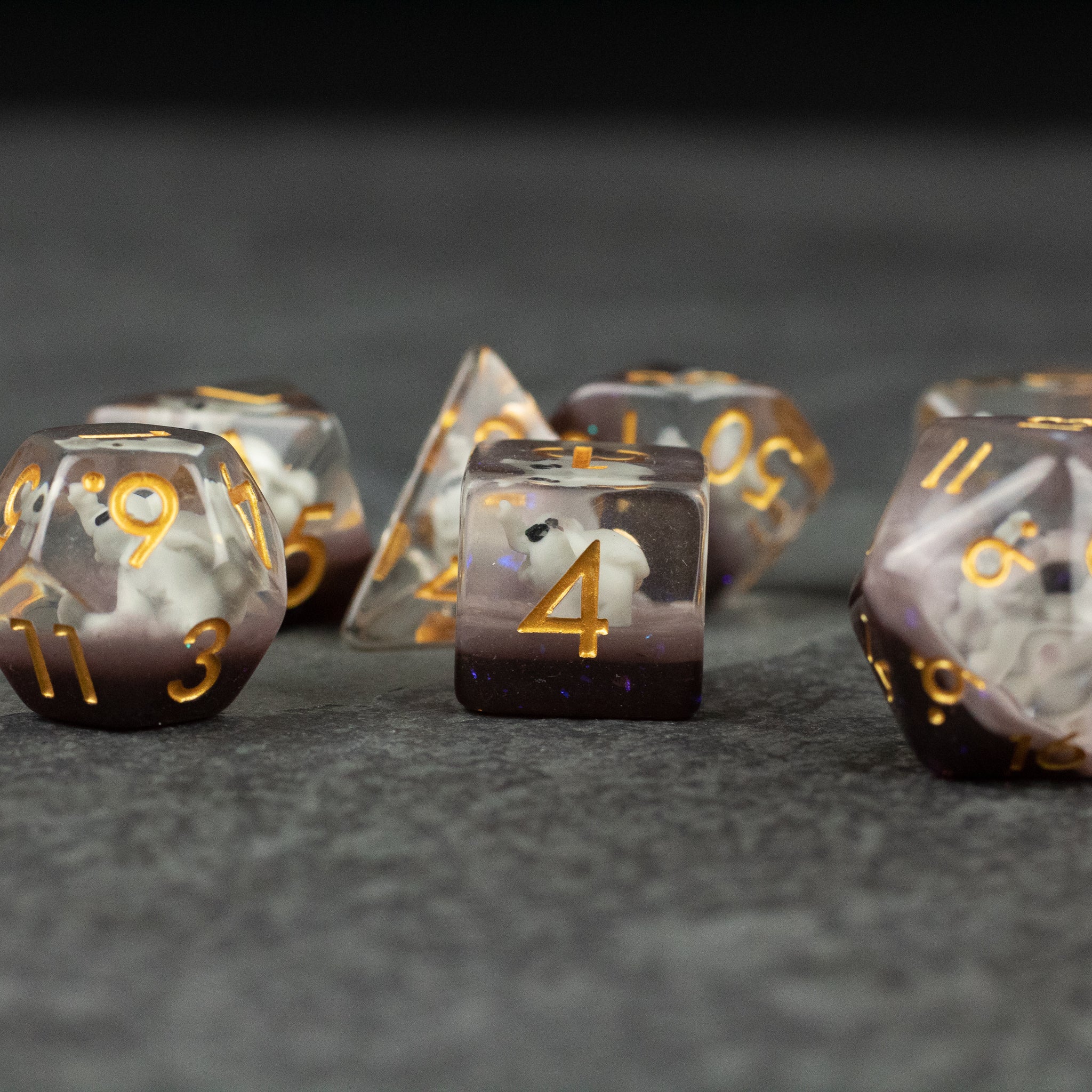 Elephant Dice Set - Set of translucent gray polyhedral dice with gold numbers and subtle elephant silhouettes inside each die.