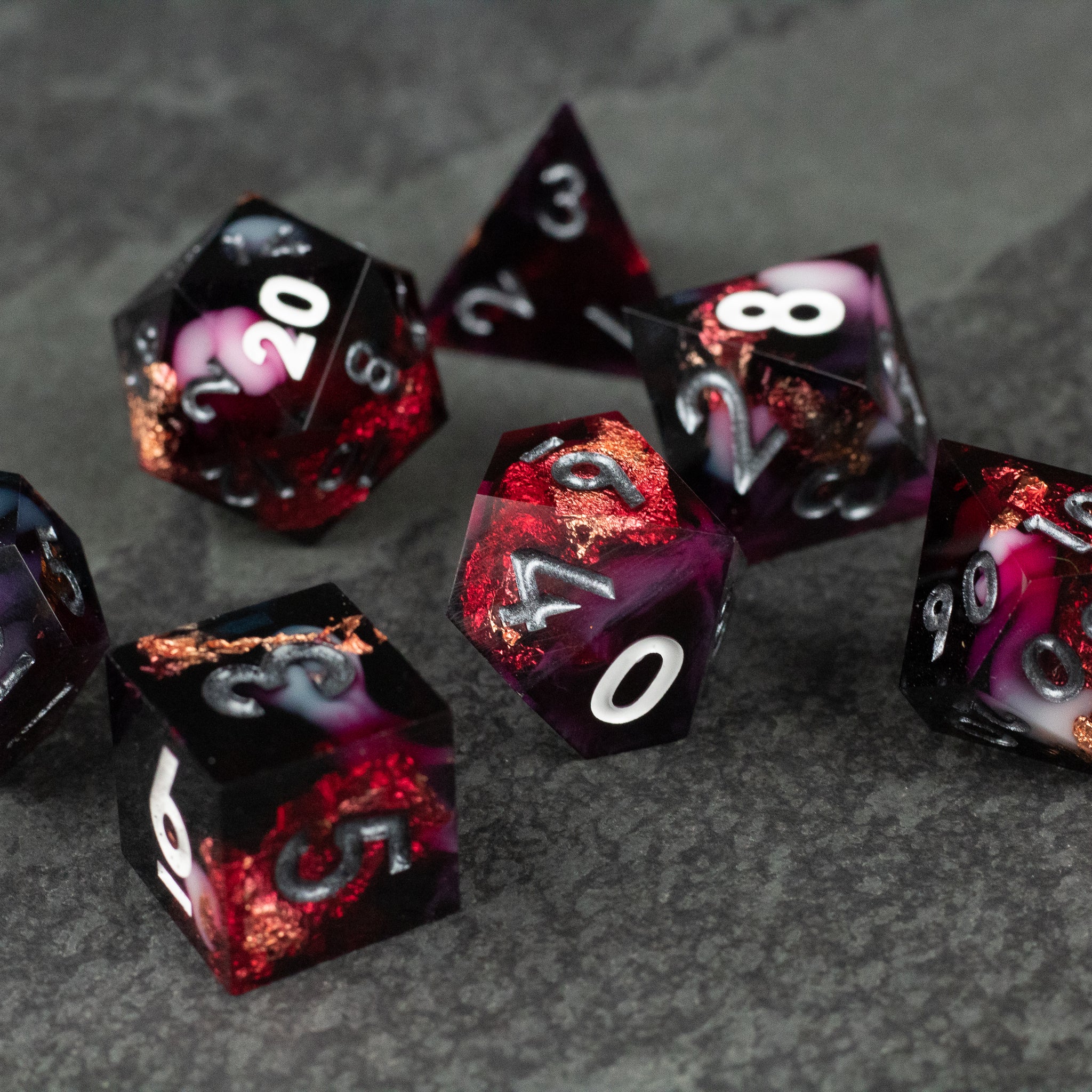 Sanguine Sacrament Dice Set - Red and black sharp-edged polyhedral dice set with white numbering on a dark stone surface.