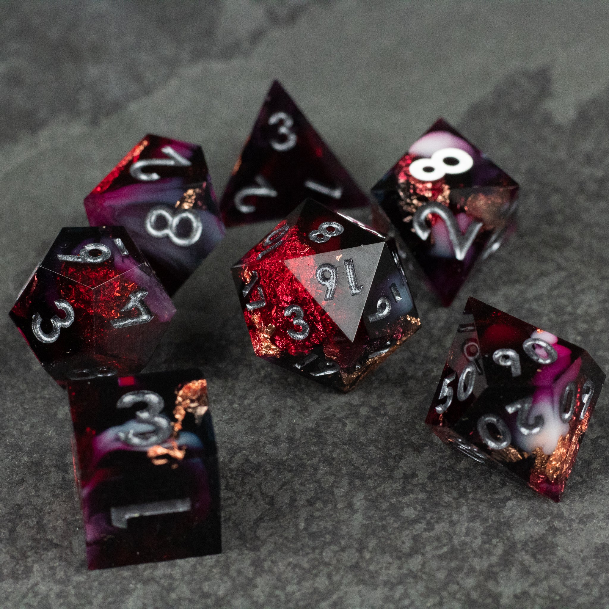 Sanguine Sacrament Dice Set - Seven sharp-edged polyhedral dice with red and black marbled design and white numbers.