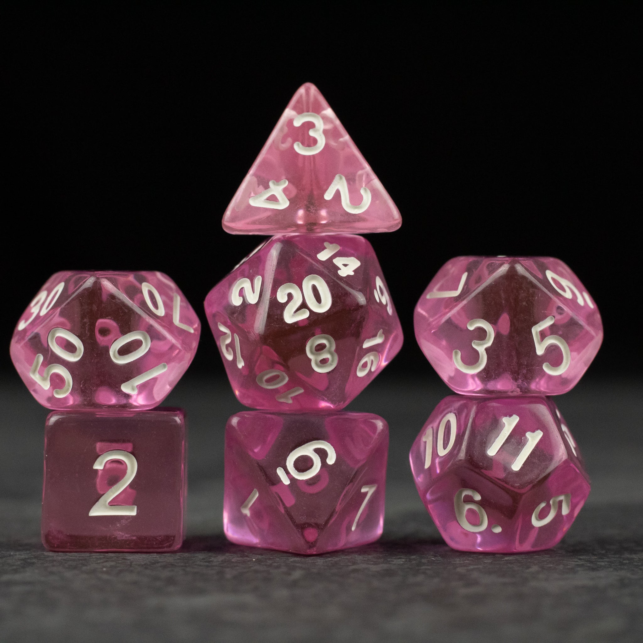 Pink Transparent Dice Set - Set of seven pink transparent polyhedral dice with white numbers, including d4, d6, d8, d10, d12, and d20 shapes.