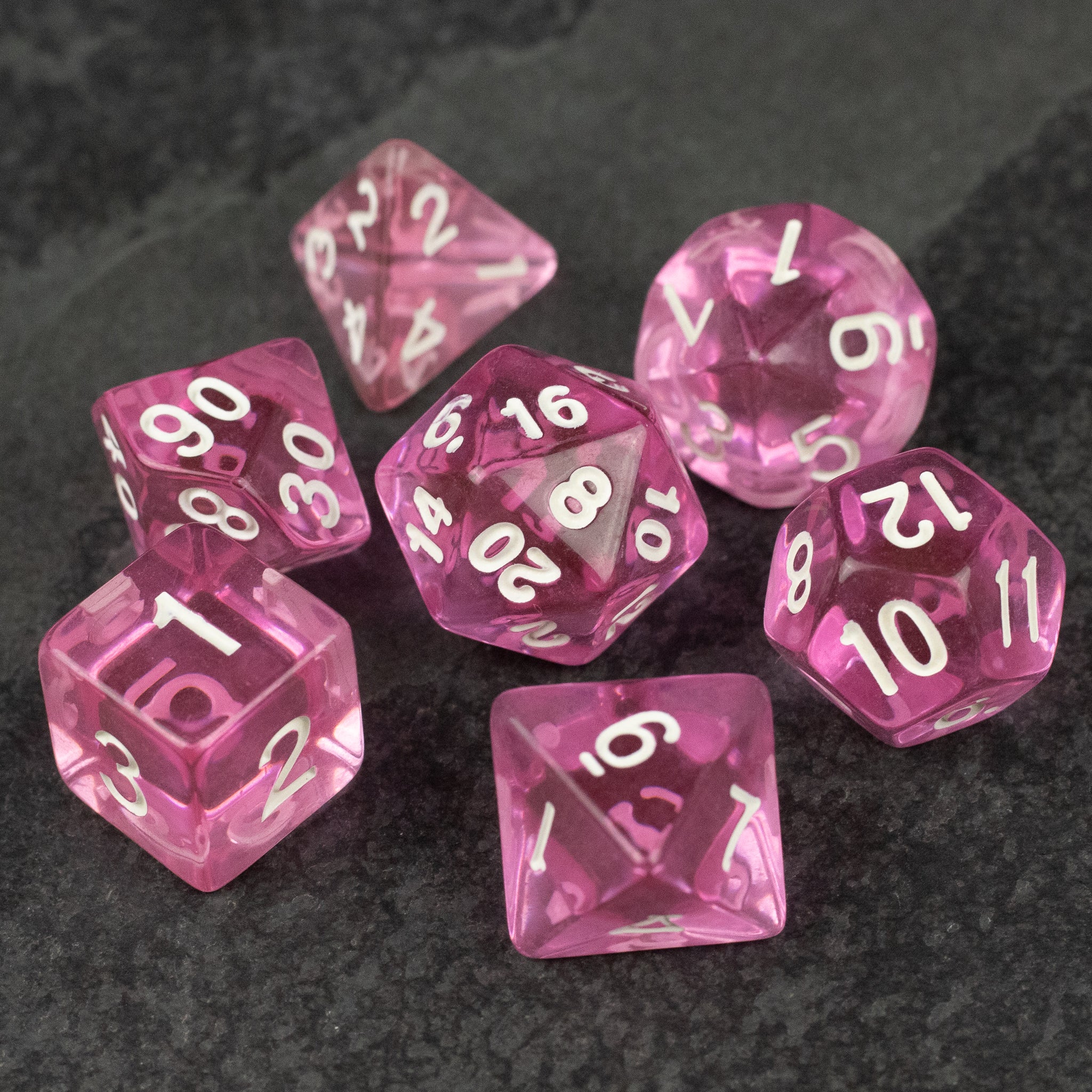 Pink Transparent Dice Set - Seven-piece pink transparent polyhedral dice set with white numbers on a dark background.
