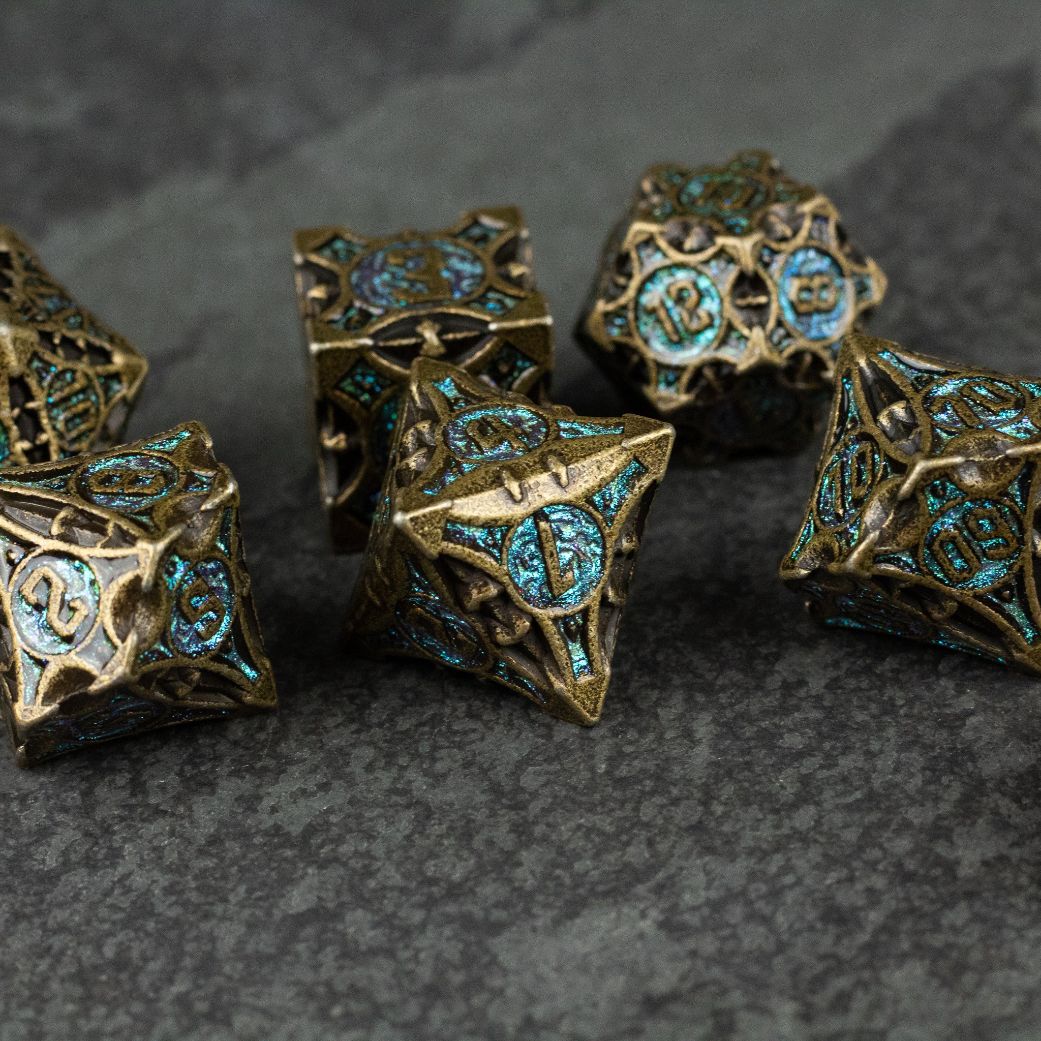 Empyrean Artifact Dice Set - Metal dice set with intricate turquoise and gold antique-style engravings on dark stone surface.