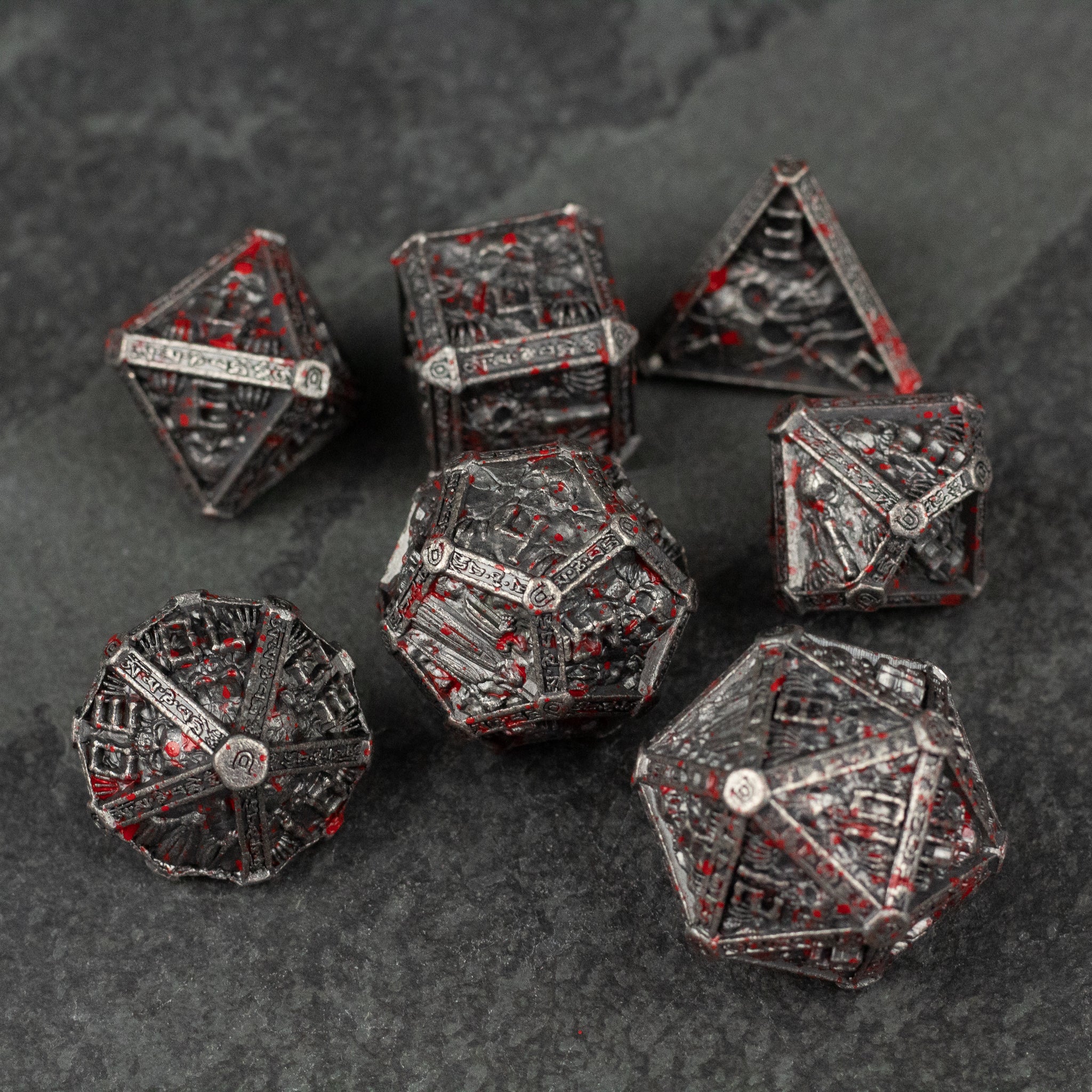 Bloody Necromancer Metal Dice Set - Set of seven metal gaming dice in dark gray with blood-red accents and intricate necromancer-themed engravings.