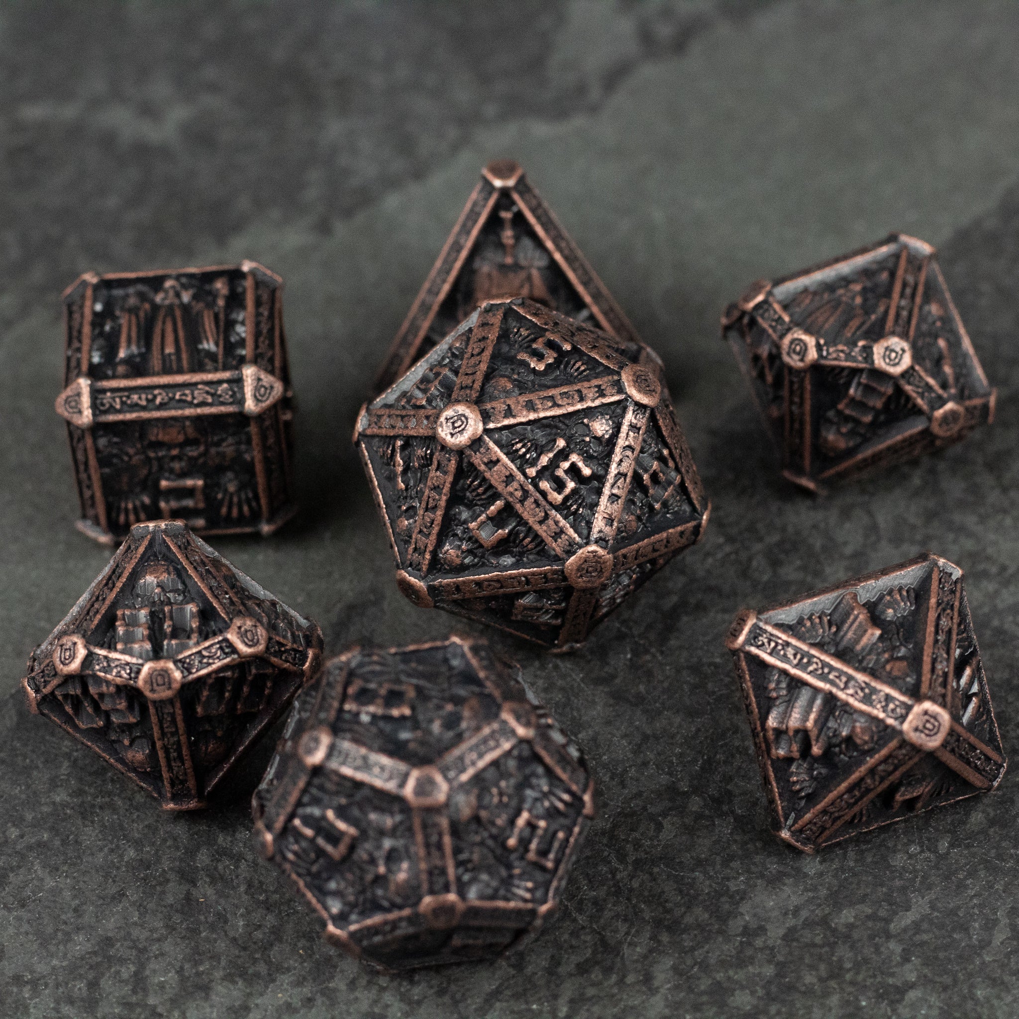 Bronze Necromancer Metal Dice Set - Seven bronze metal dice with intricate necromancer-style engravings on a dark stone surface.
