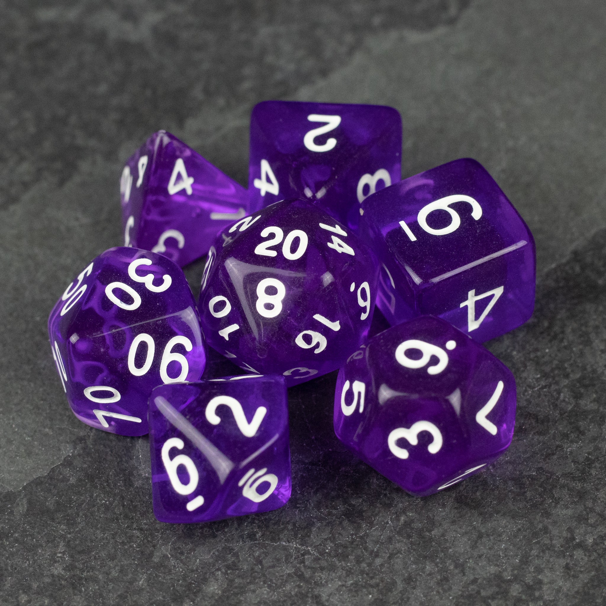 Purple Transparent Dice Set - Set of seven purple transparent polyhedral dice with white numbering on a dark gray surface.