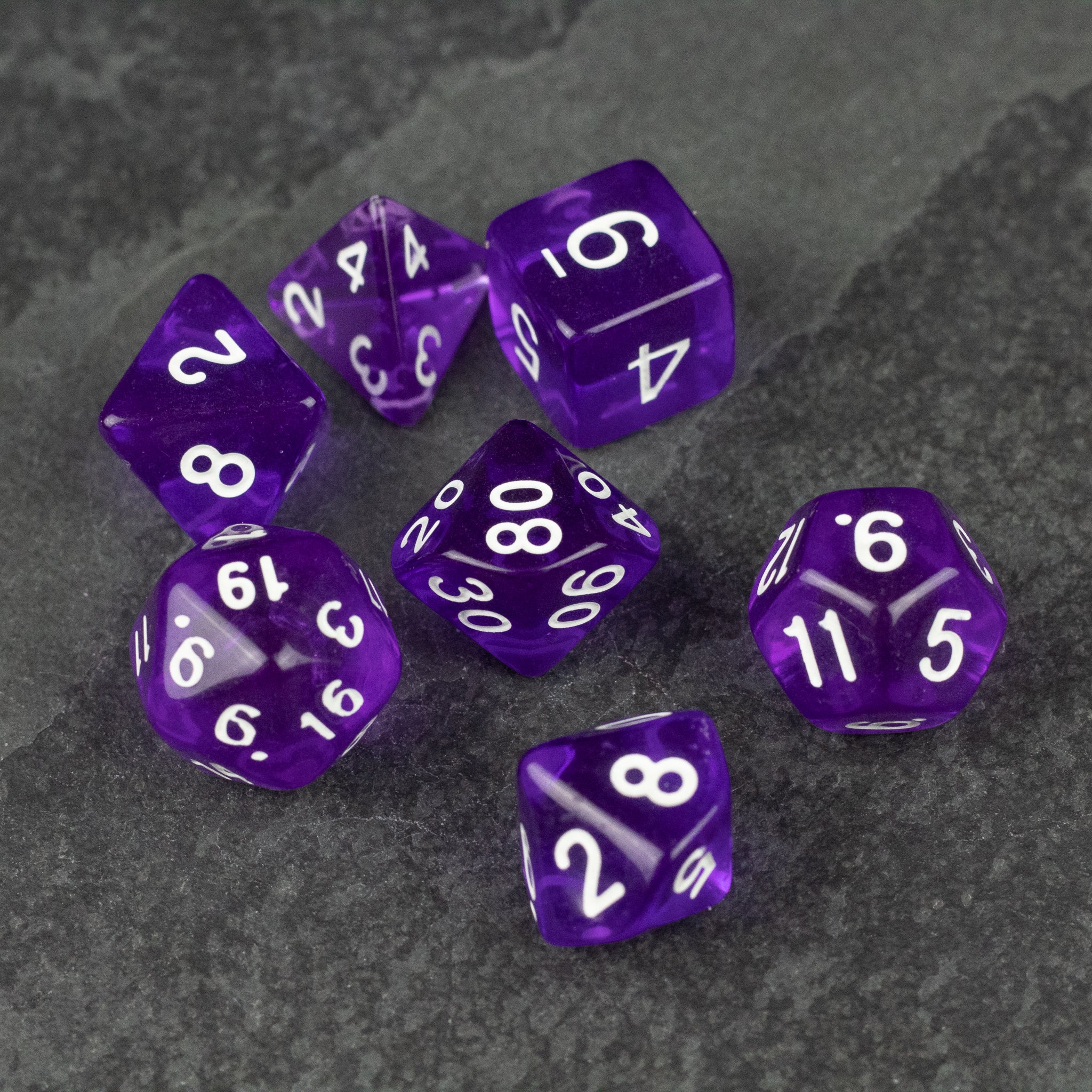 Purple Transparent Dice Set - Set of seven purple transparent dice with white numbers on a dark textured surface.