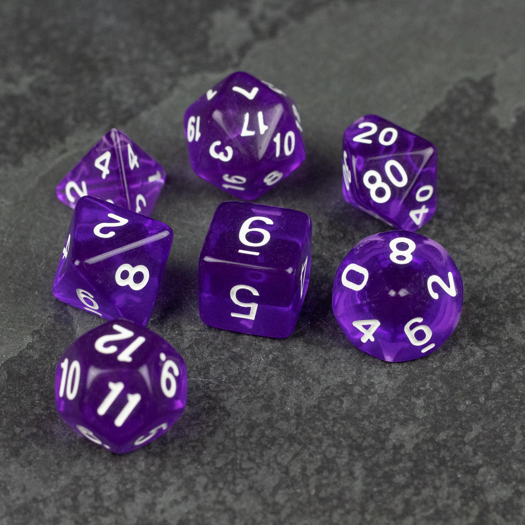 Purple Transparent Dice Set - Seven purple transparent polyhedral dice with white numbering on dark gray surface.