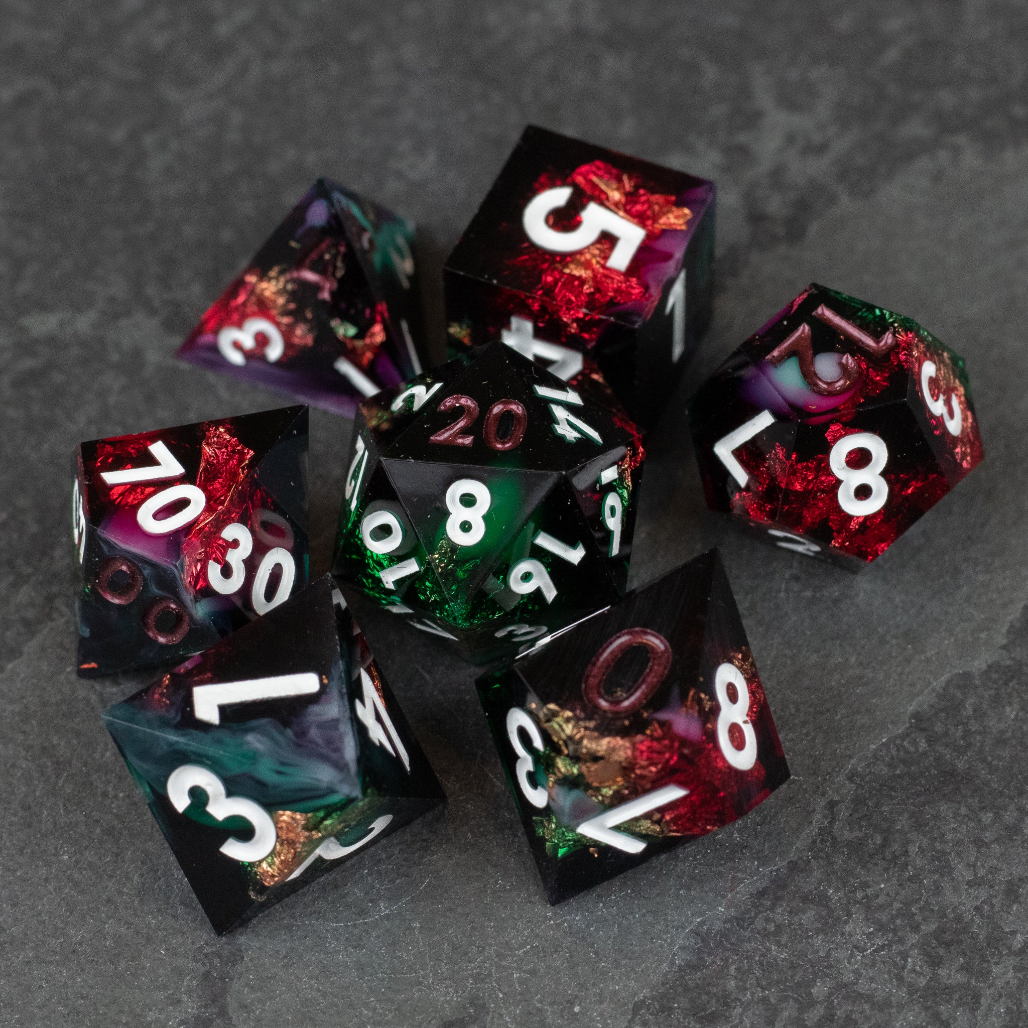 Chromatic Aberration Dice Set - Set of seven sharp-edged polyhedral dice, translucent with swirling black, red, and green colors, white numbers.