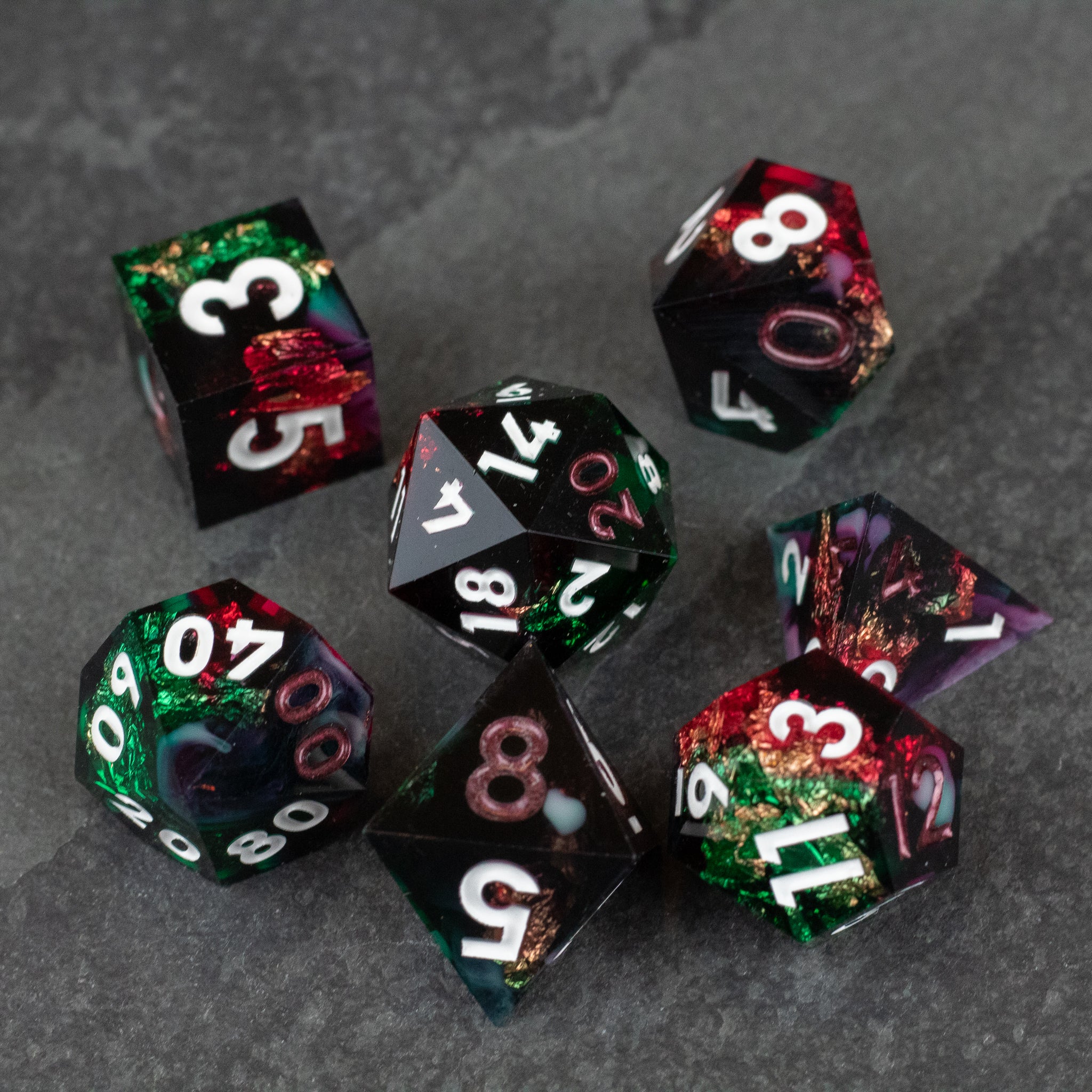 Chromatic Aberration Dice Set - Set of seven sharp-edged polyhedral dice with a glossy, multicolored design featuring deep greens, reds, and blacks, white.