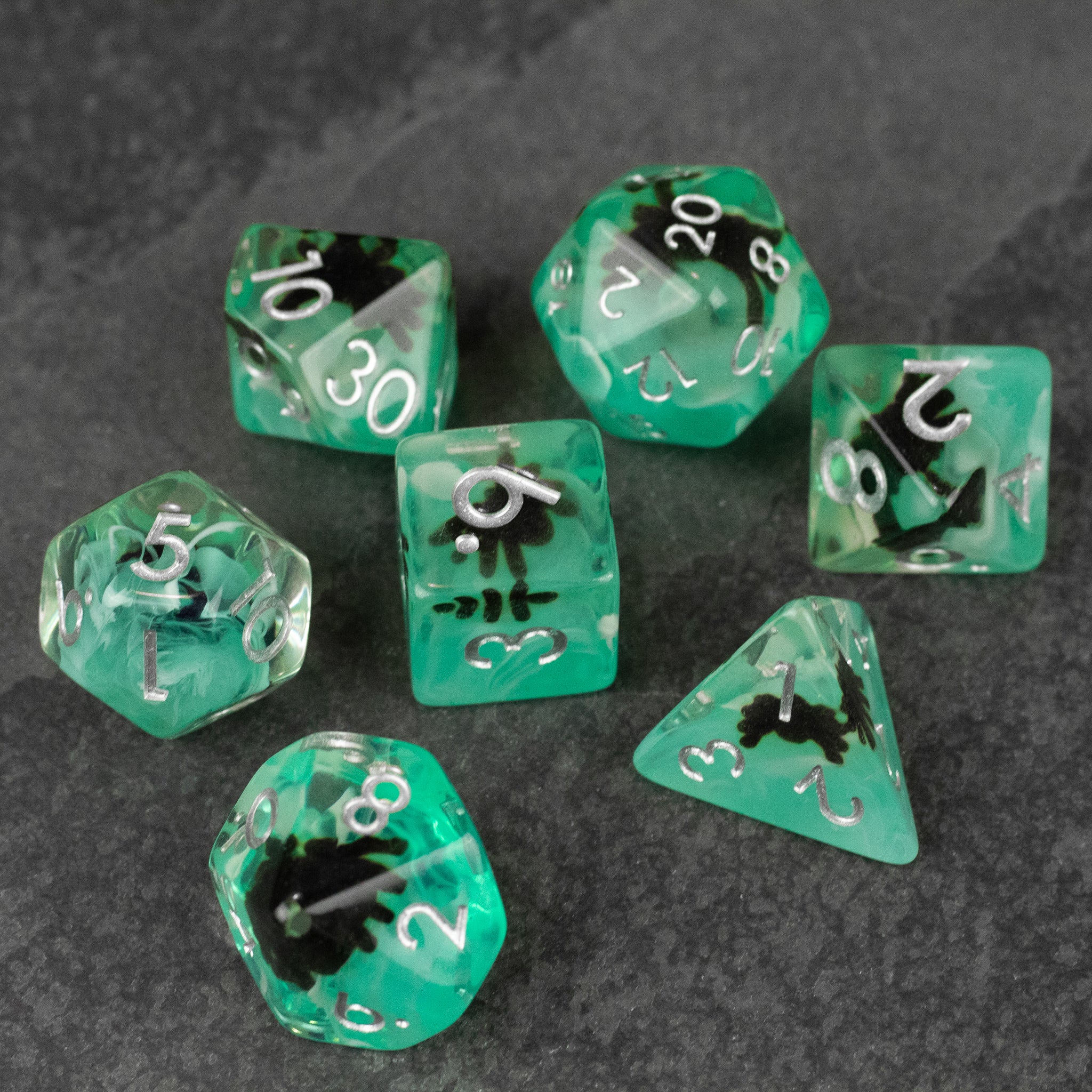 Black Spider Dice Set - Green - Translucent green seven-piece dice set with black spider designs and white numbering on a dark background.