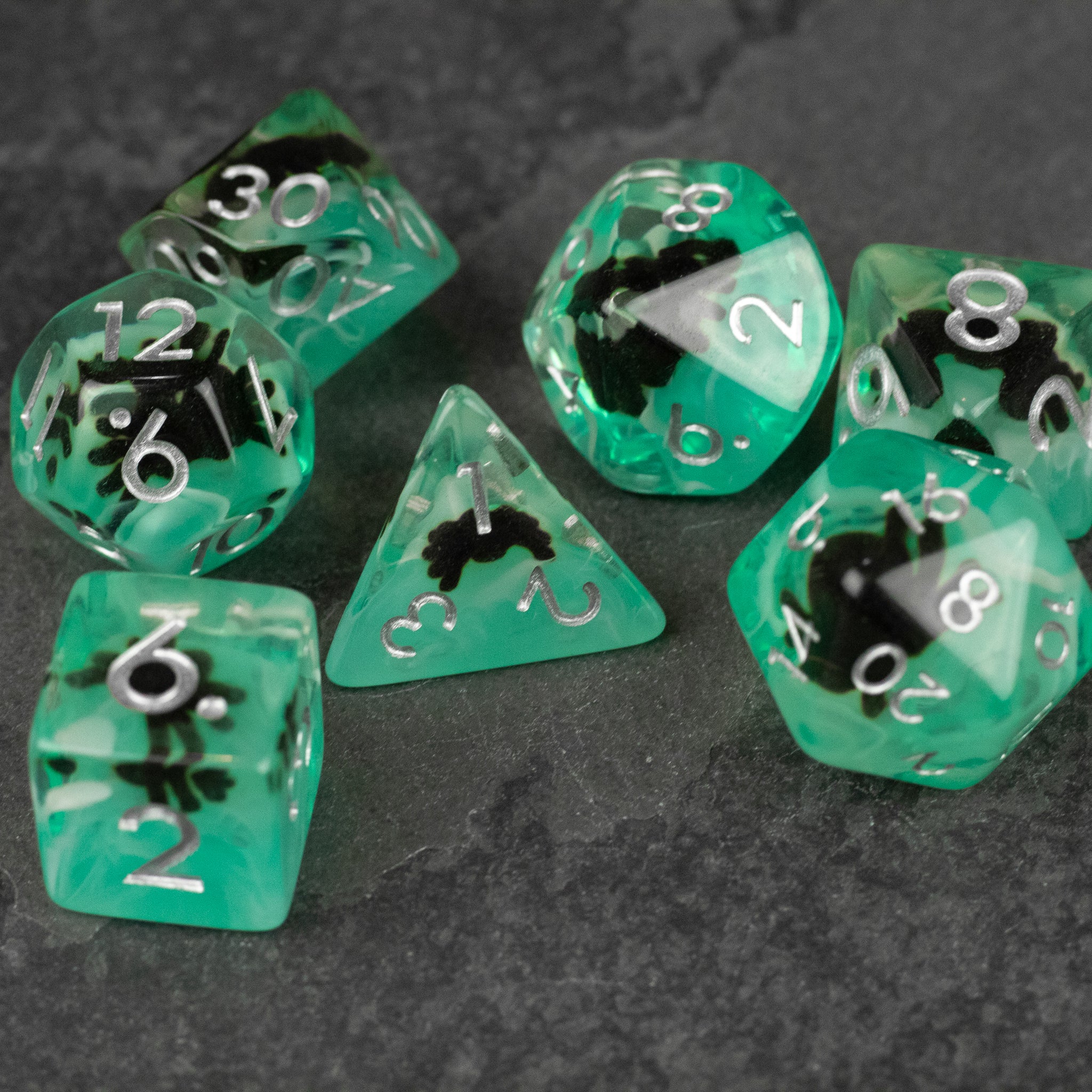 Black Spider Dice Set - Green - Seven green translucent polyhedral dice with white numbers and black spider silhouettes inside each die on a dark textured.