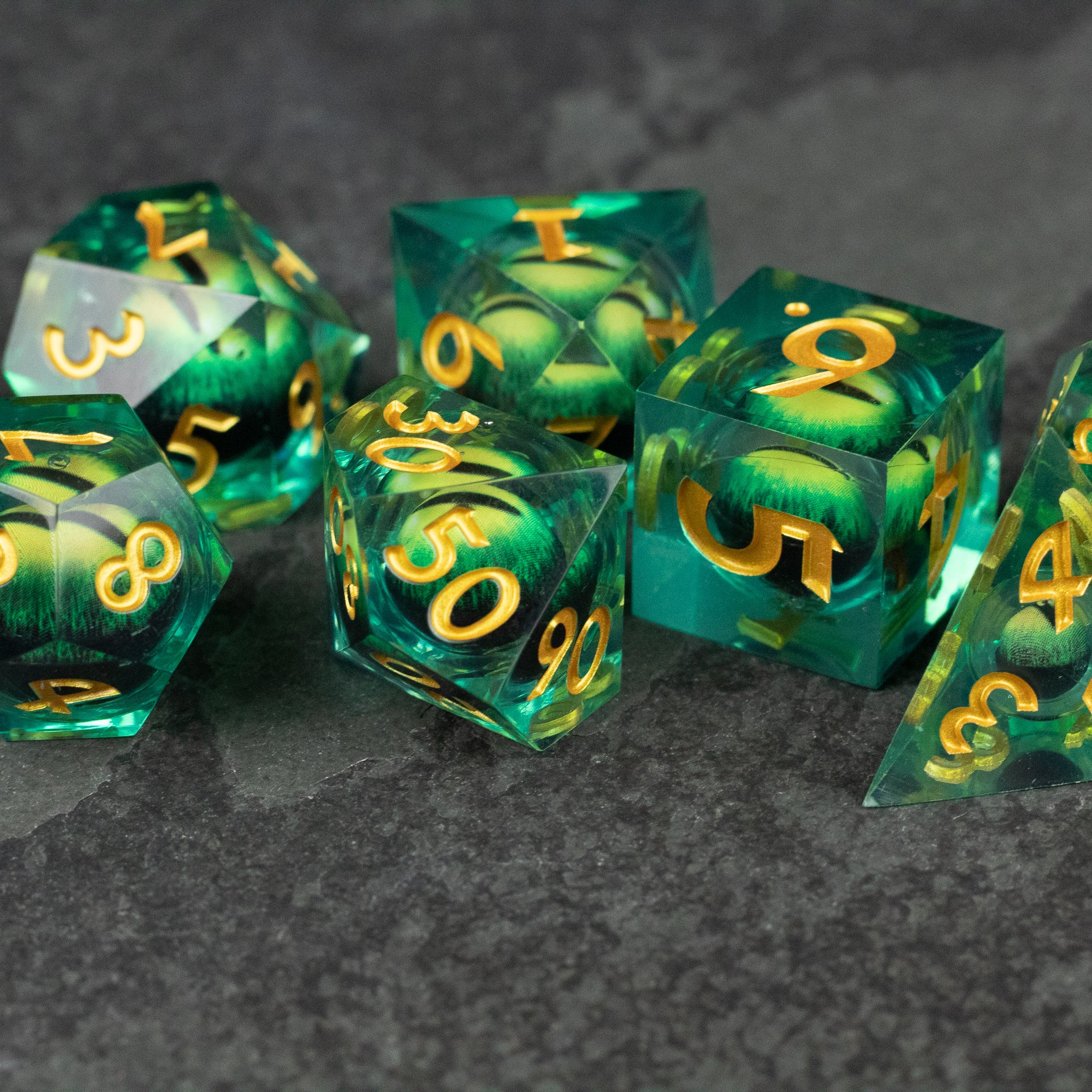 Green Beholder's Eye Dice Set - Green translucent polyhedral dice set with swirling liquid core and gold numbers, sharp edges.