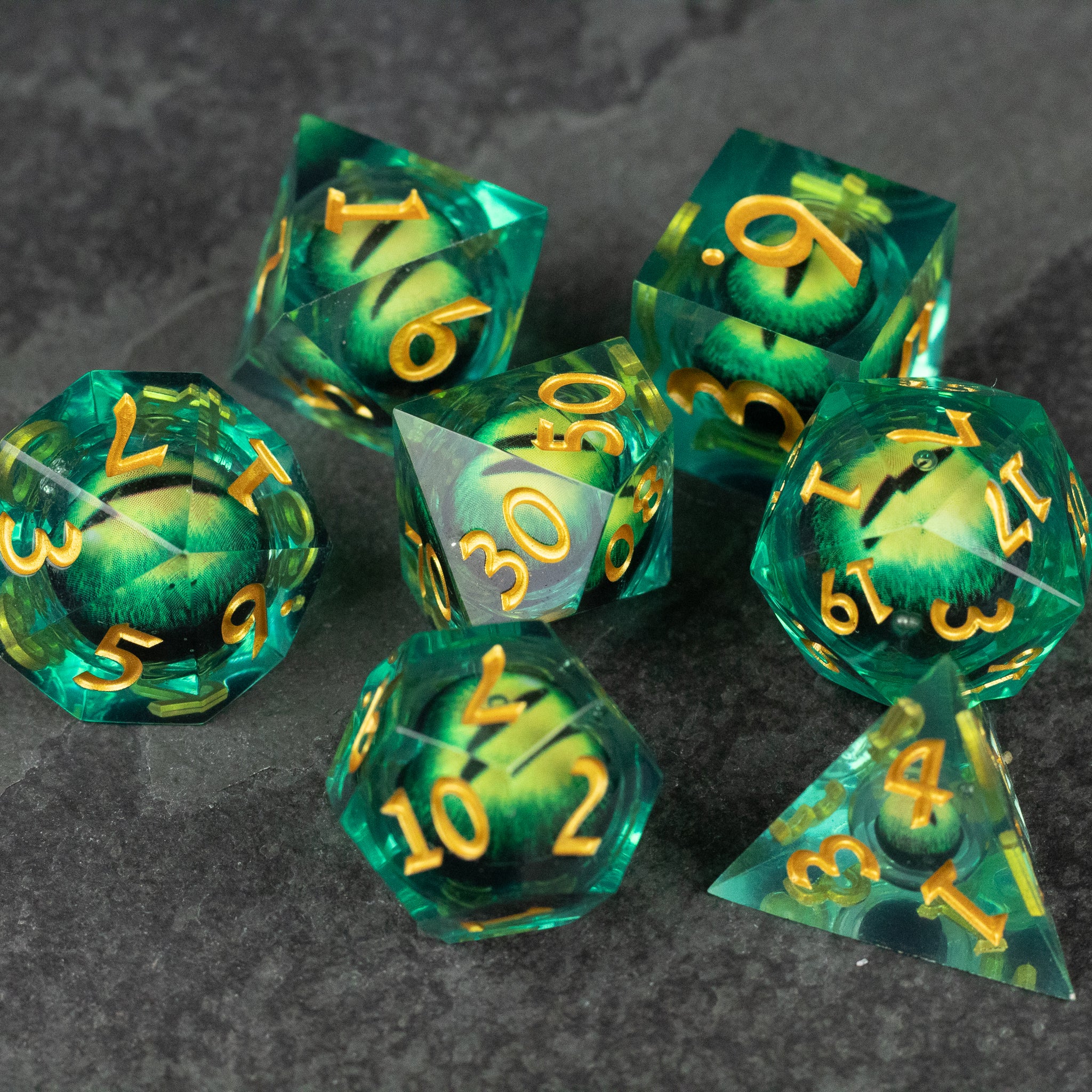 Green Beholder's Eye Dice Set - Set of seven translucent green polyhedral dice with gold numbers and liquid core, sharp edges.