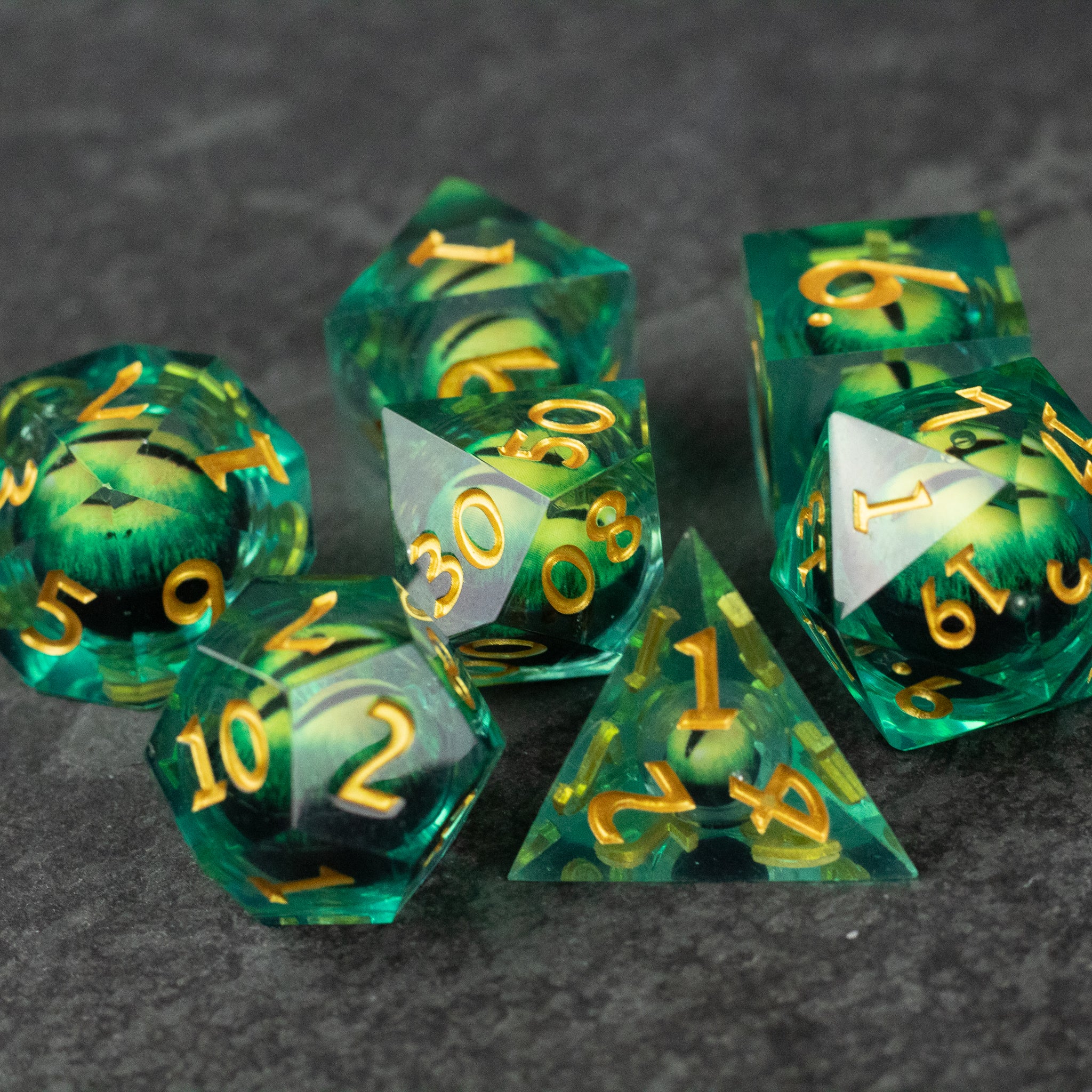 Green Beholder's Eye Dice Set - Green translucent polyhedral dice set with gold numbers and liquid-like core, sharp edges.