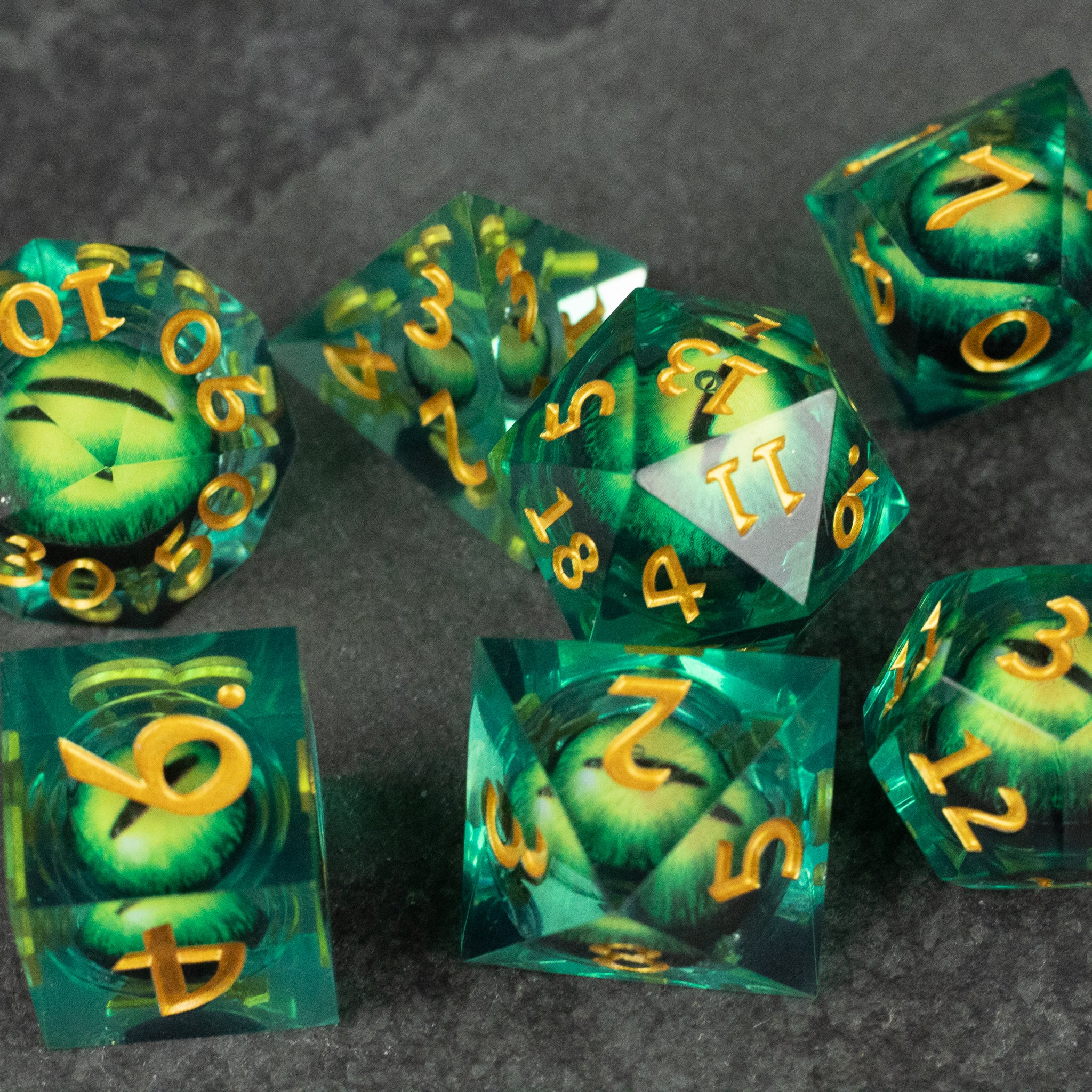 Green Beholder's Eye Dice Set - Translucent green polyhedral dice set with sharp edges and gold numbering featuring swirling liquid core designs.