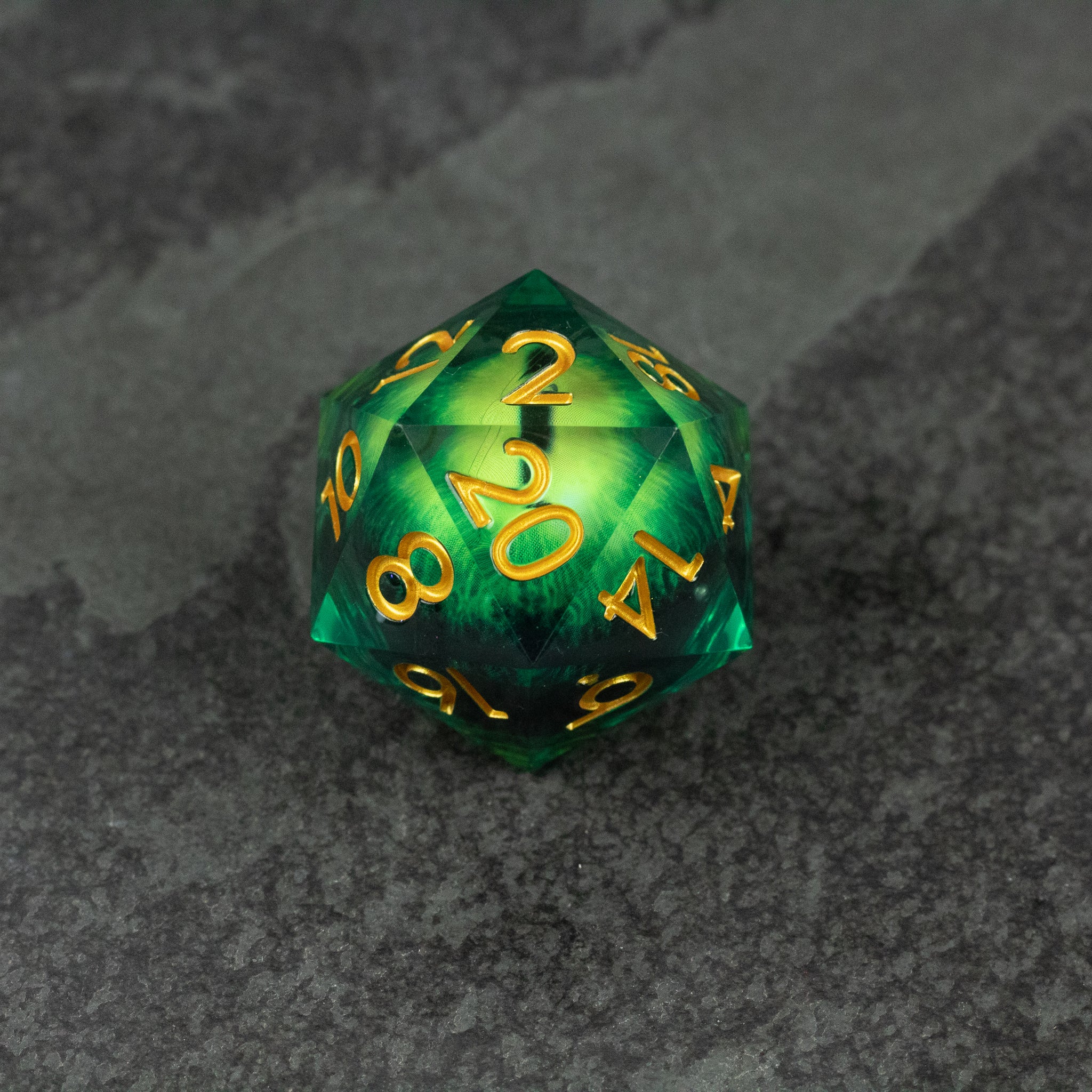 33mm Liquid Floating Eye - Green - Green 33mm icosahedron die with gold numbers and liquid core design on dark stone surface.